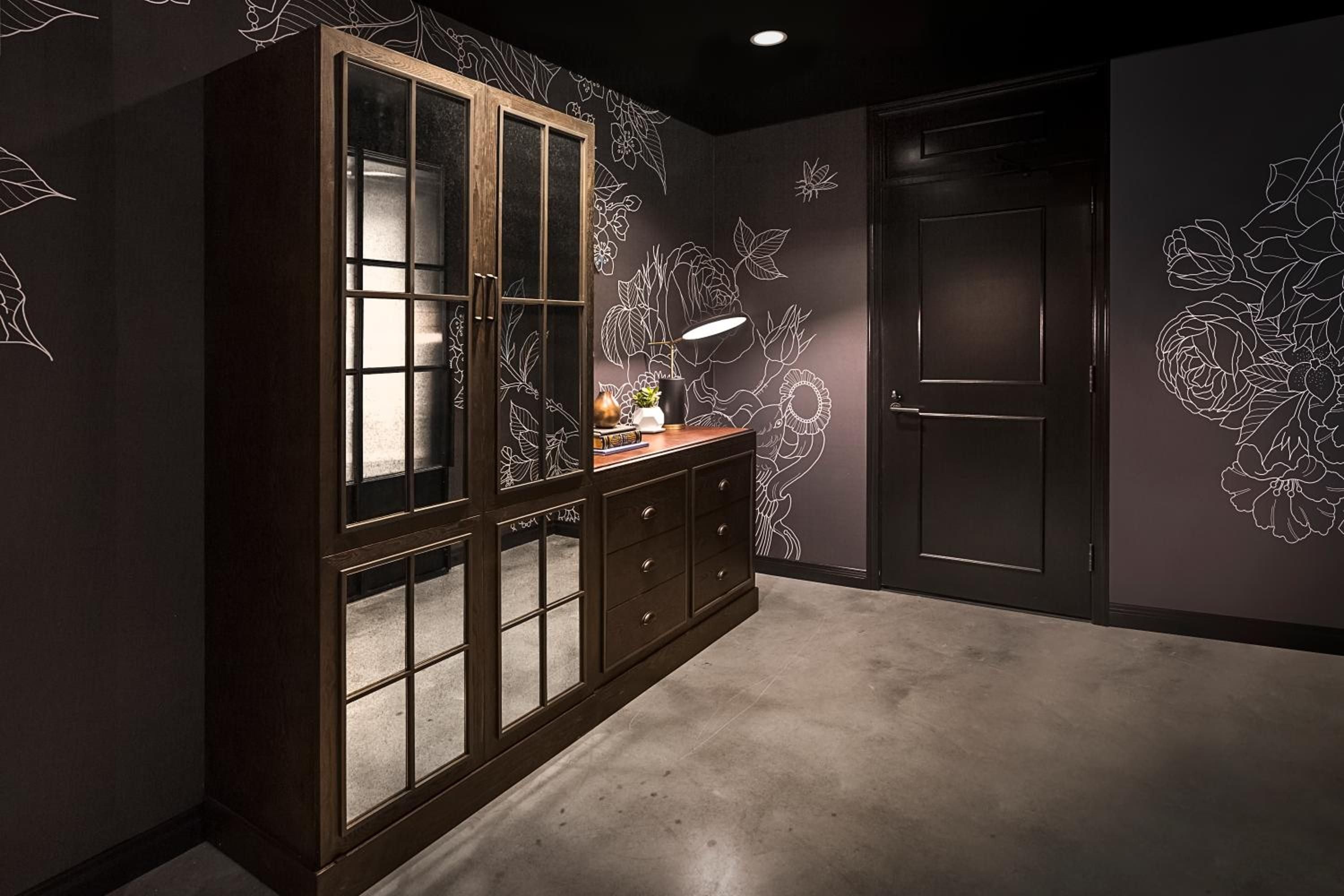 Hand-drawn botanical murals bloom across charcoal walls in this moody corridor, where warm wood cabinetry and concrete floors create an artful blend of sophistication and creative spirit.