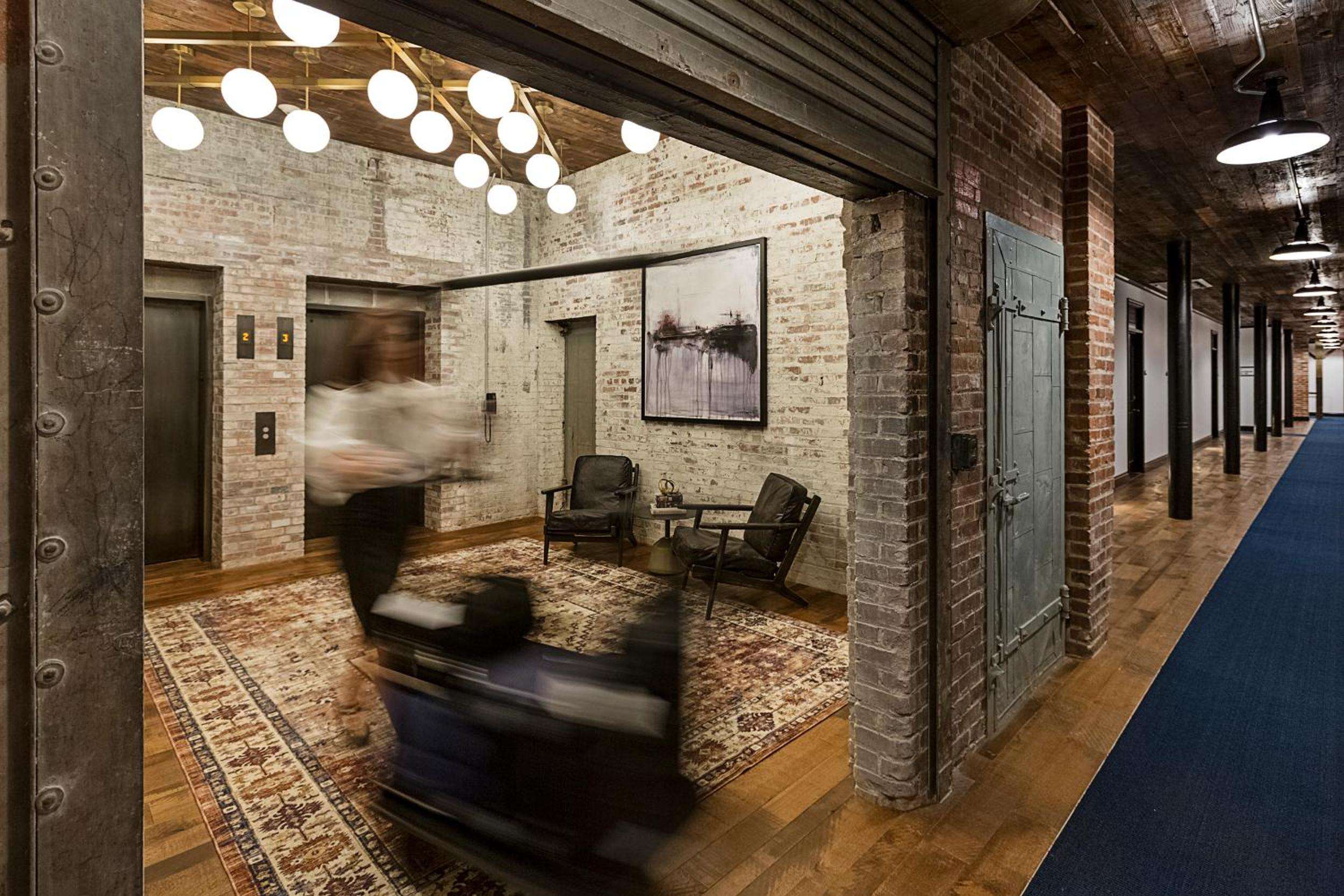 Exposed brick walls and industrial beams frame intimate seating vignettes, where globe lights cast warm shadows across weathered leather chairs and Persian rugs.
