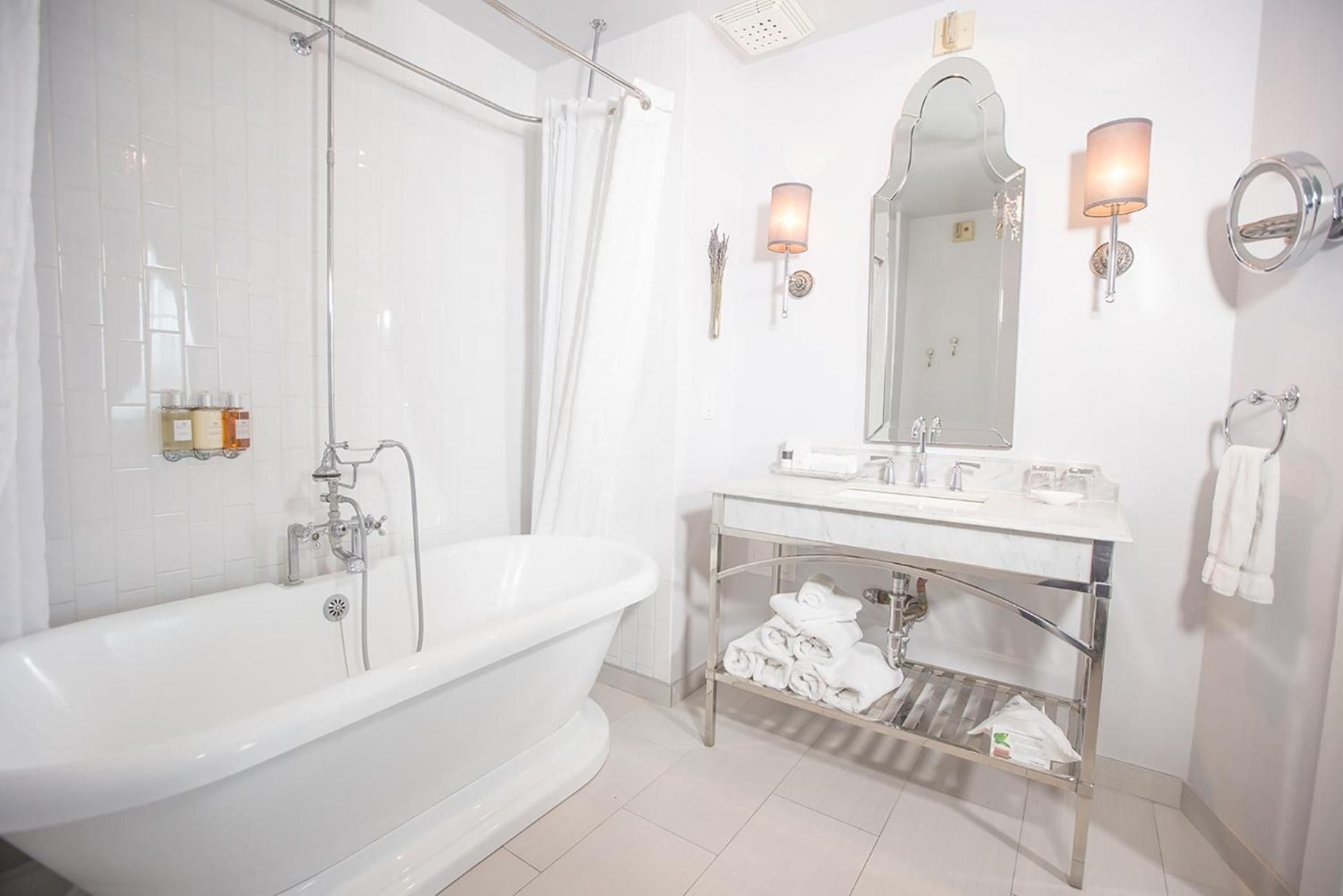 Marble surfaces gleam under warm sconces while vintage-inspired fixtures and an open vanity design create an airy, sophisticated bathing retreat.