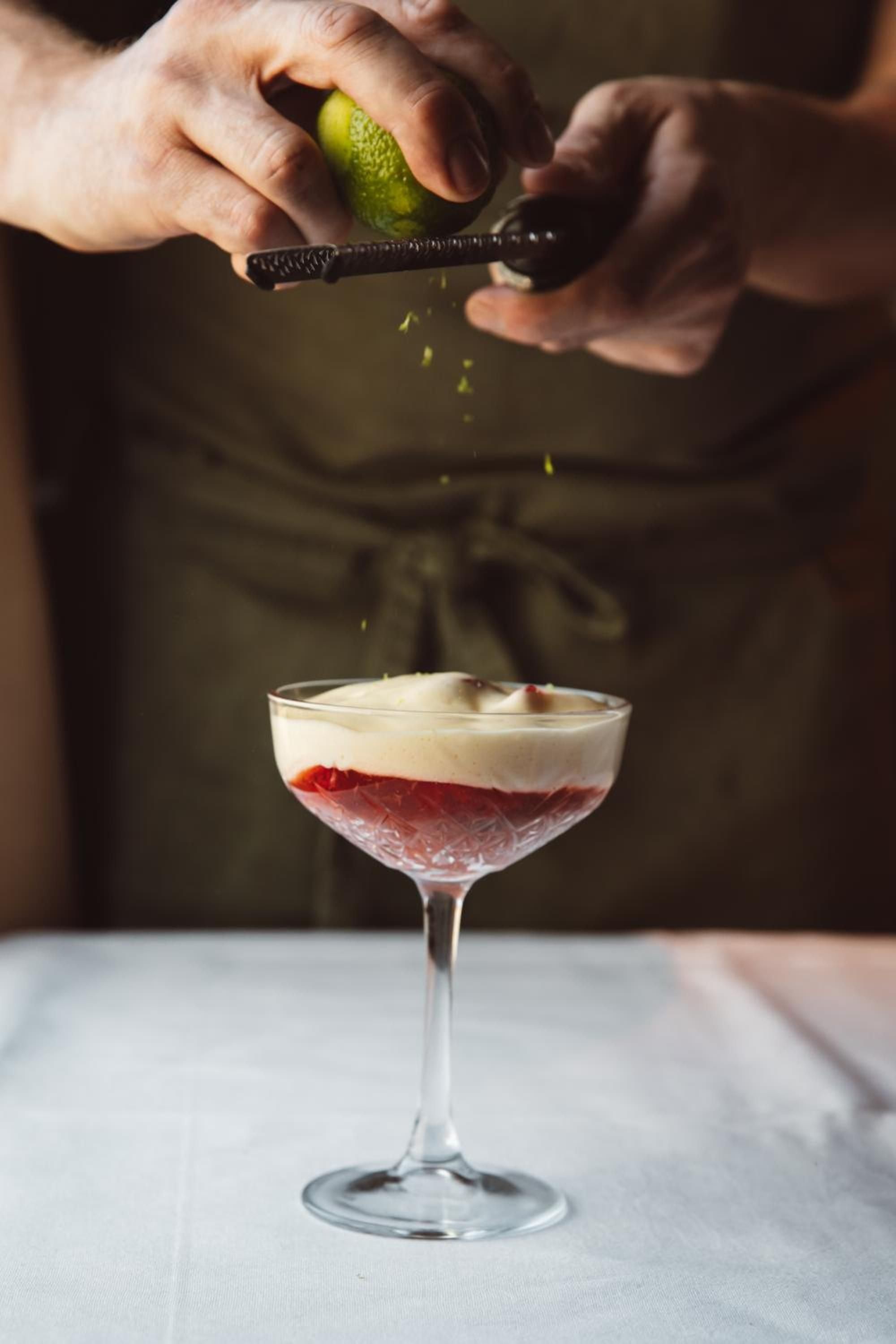 Fresh lime zest cascades into a perfectly layered cocktail as skilled bartenders craft artisanal drinks with theatrical precision and aromatic flourishes.