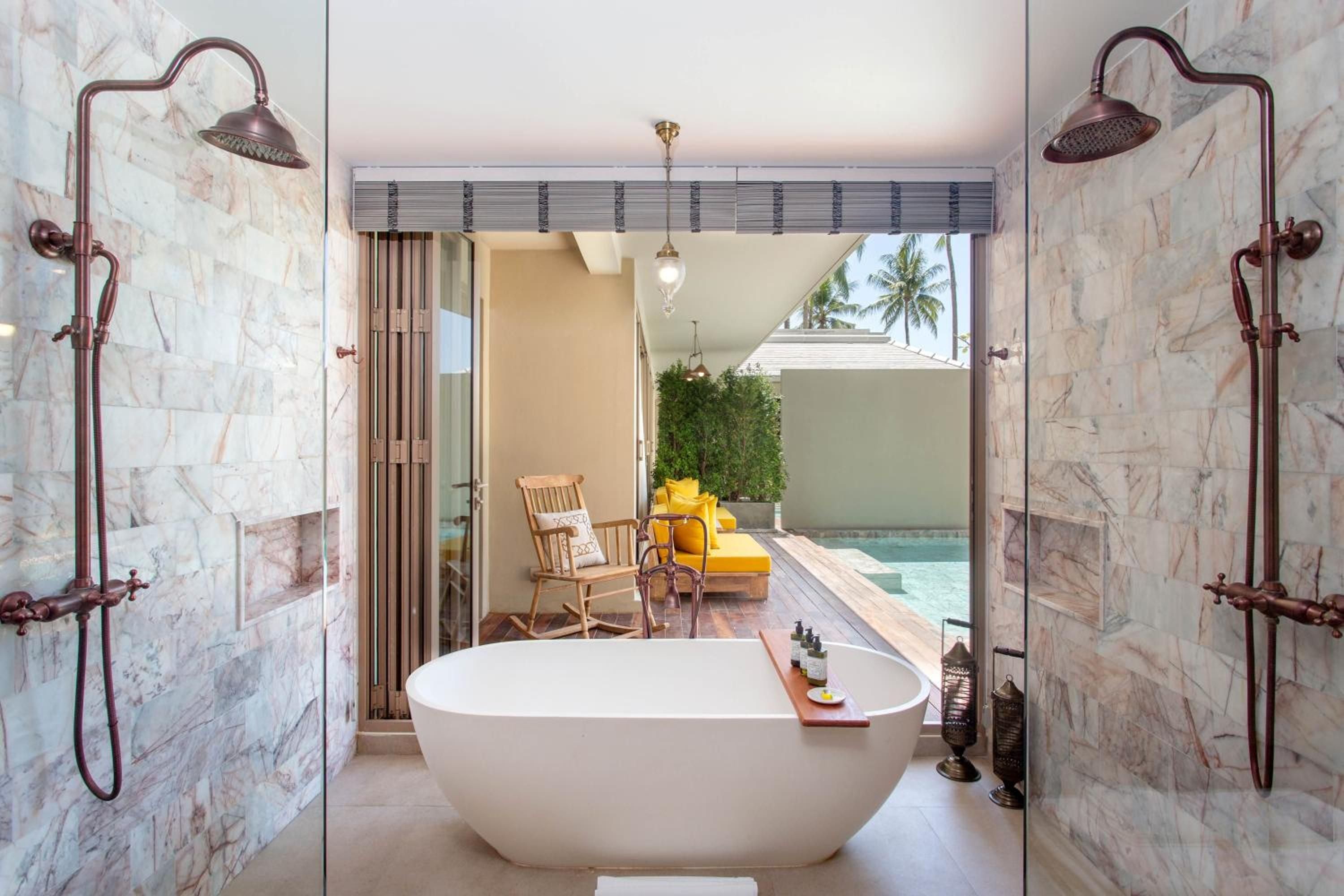 Copper rainfall showers frame a sculptural soaking tub where Carrara marble meets turquoise pool views, creating an open-air sanctuary that blurs indoor luxury with tropical serenity.