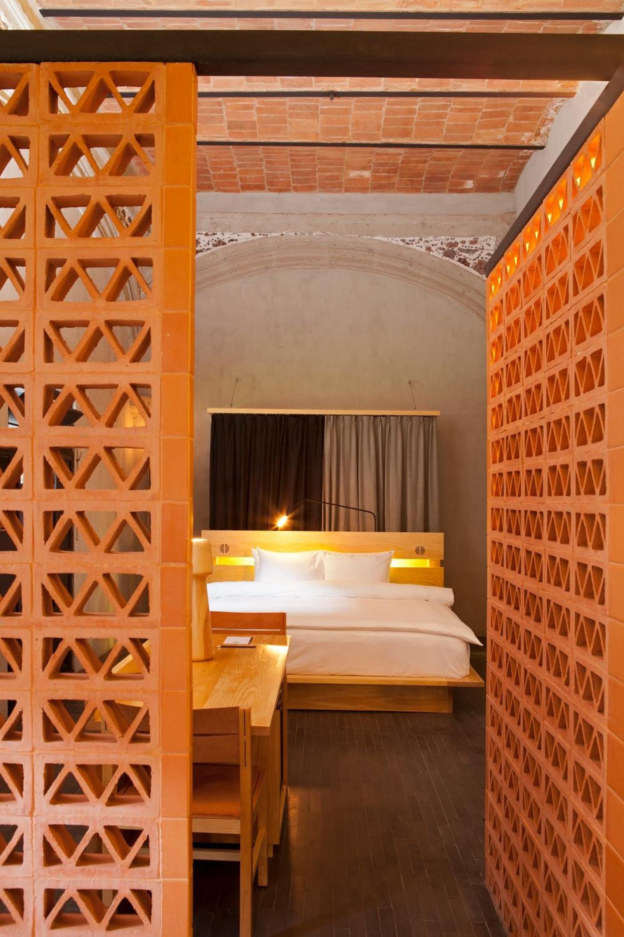 Geometric terracotta screens filter golden light into this cocoon-like bedroom, where traditional Mexican craftsmanship meets contemporary minimalism in perfect harmony.