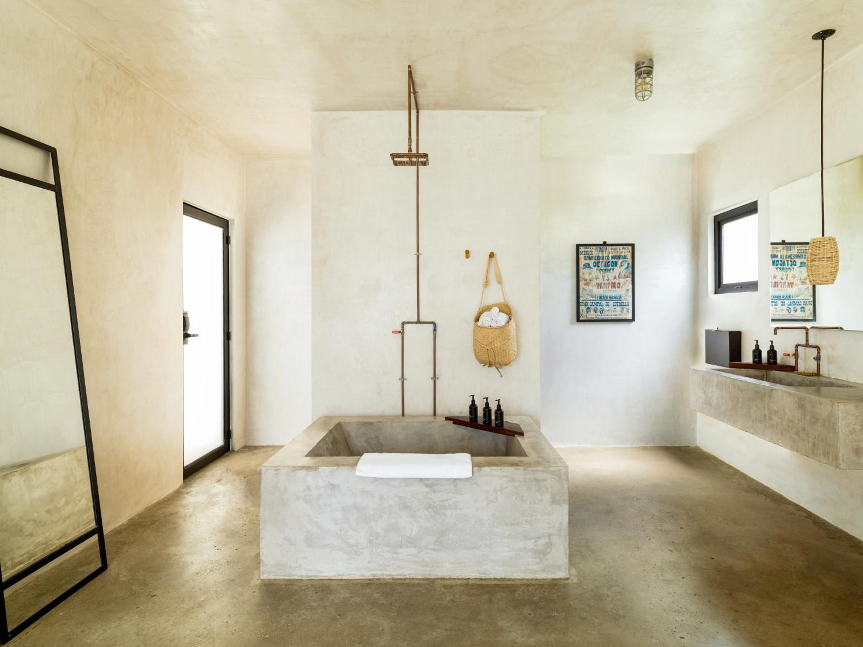 Polished concrete and raw textures define this sanctuary-like bathroom, where a sculptural soaking tub anchors the minimalist space beneath industrial-chic exposed beams.