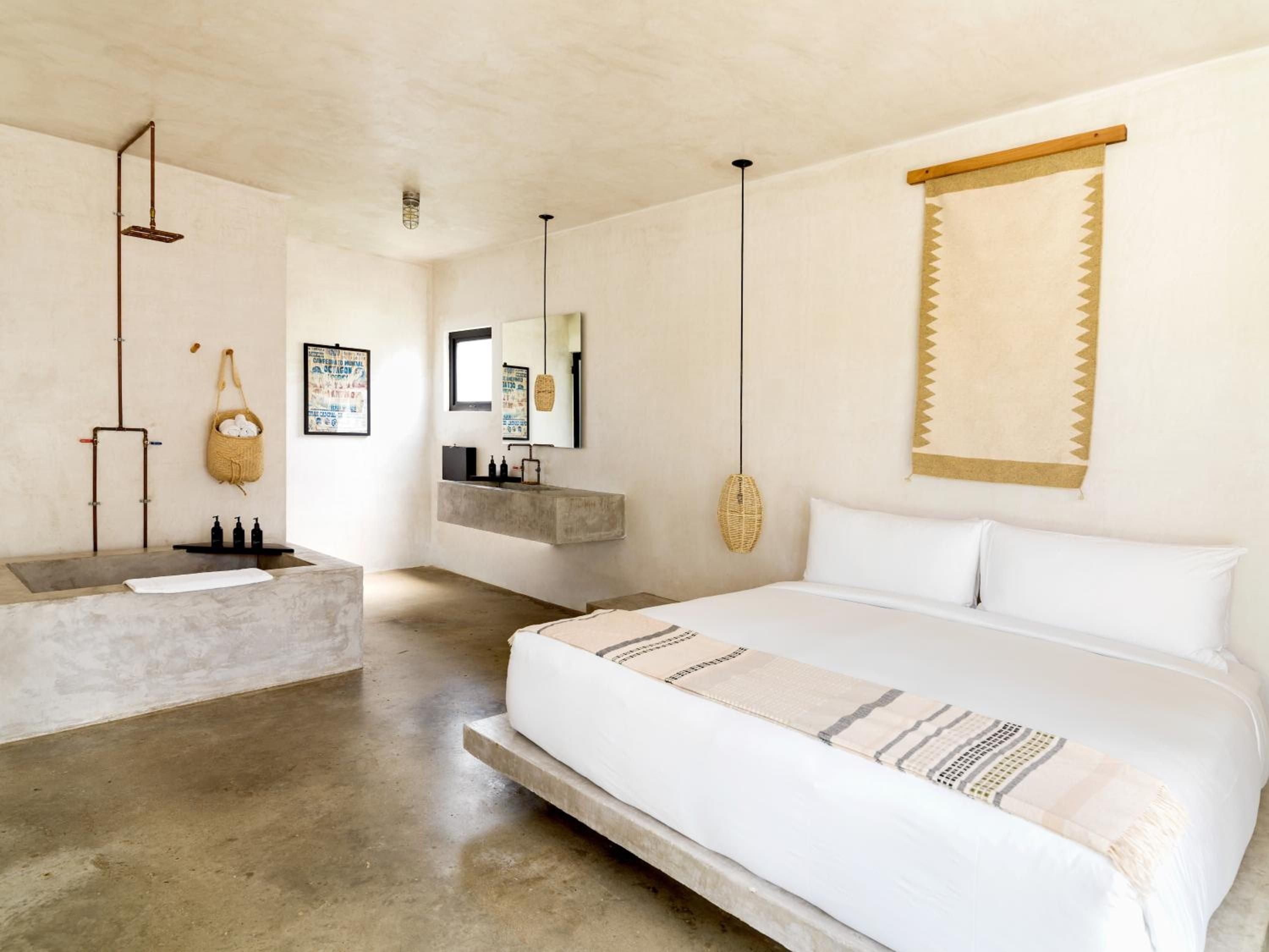Concrete floors and woven textures create serene minimalism in this suite, where pendant lighting casts gentle shadows over the integrated bathtub and curated artworks.