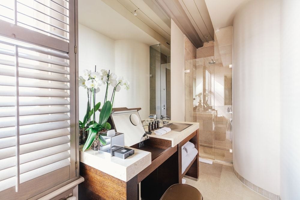Natural light filters through wooden shutters, illuminating marble surfaces and fresh orchids in this serene bathroom where modern luxury meets understated Dutch elegance.