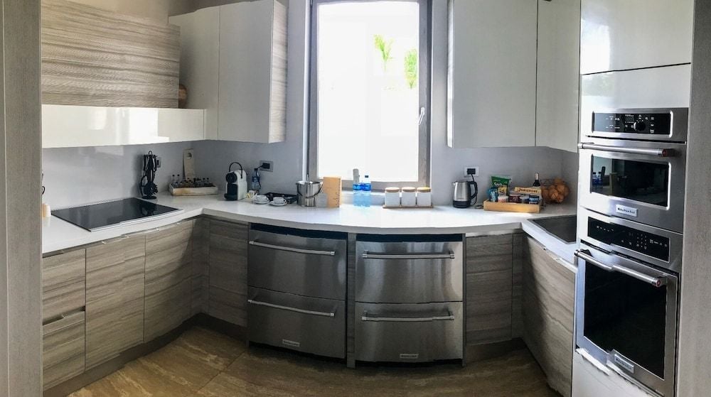 Sleek wood-grain cabinetry and pristine white countertops create a sophisticated culinary sanctuary, where stainless steel appliances gleam beneath filtered Caribbean light streaming through shuttered windows.