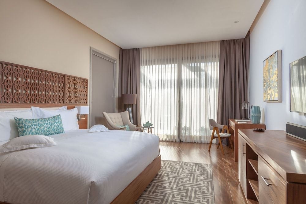 Warm wood tones and intricate carved headboards create an intimate sanctuary, where morning light filters through sheer curtains onto polished floors and geometric rugs.