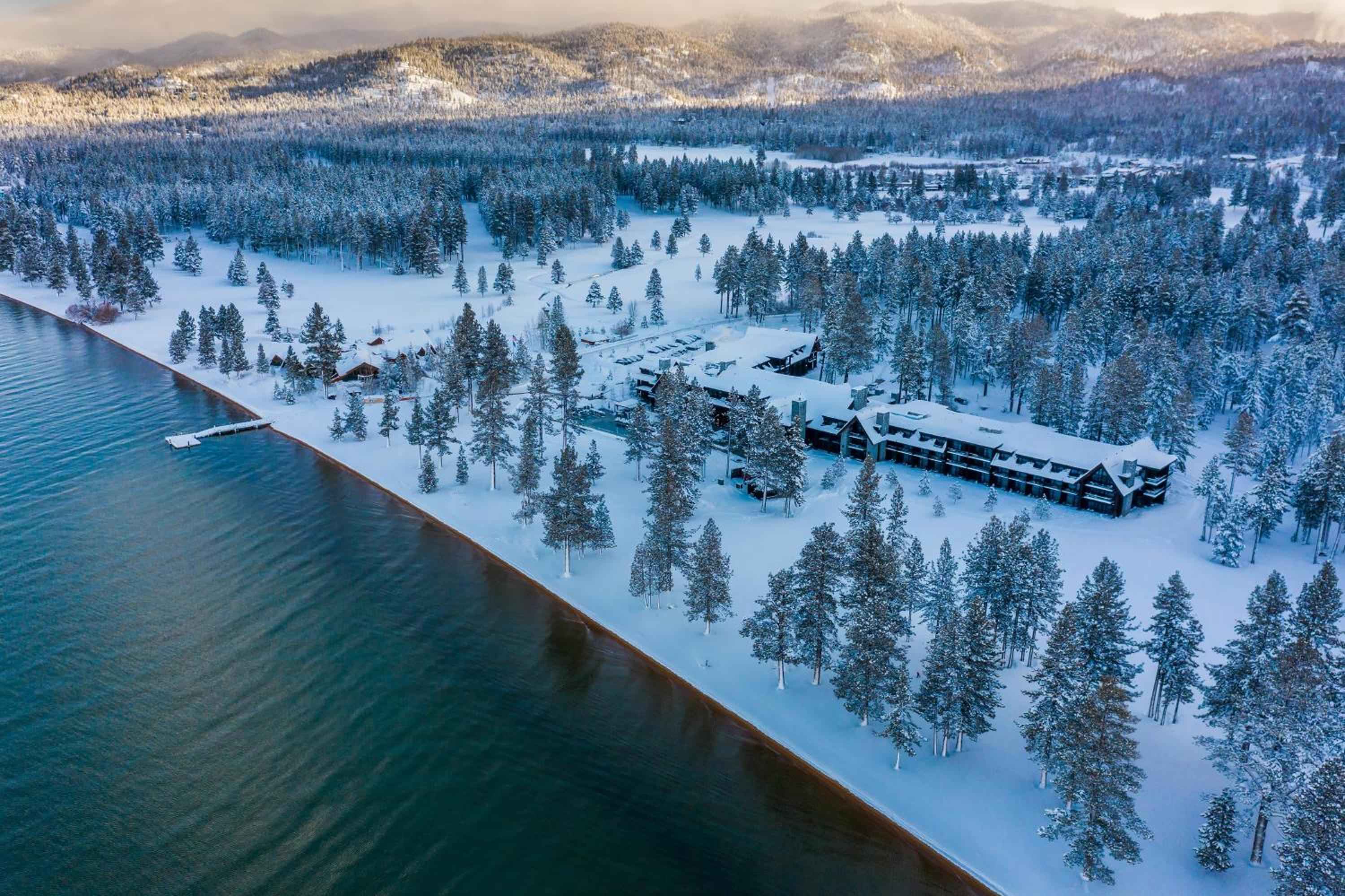 Snow-blanketed pines frame Edgewood Tahoe's lakefront lodge, where frosted timber meets crystalline waters beneath the Sierra Nevada's winter embrace.