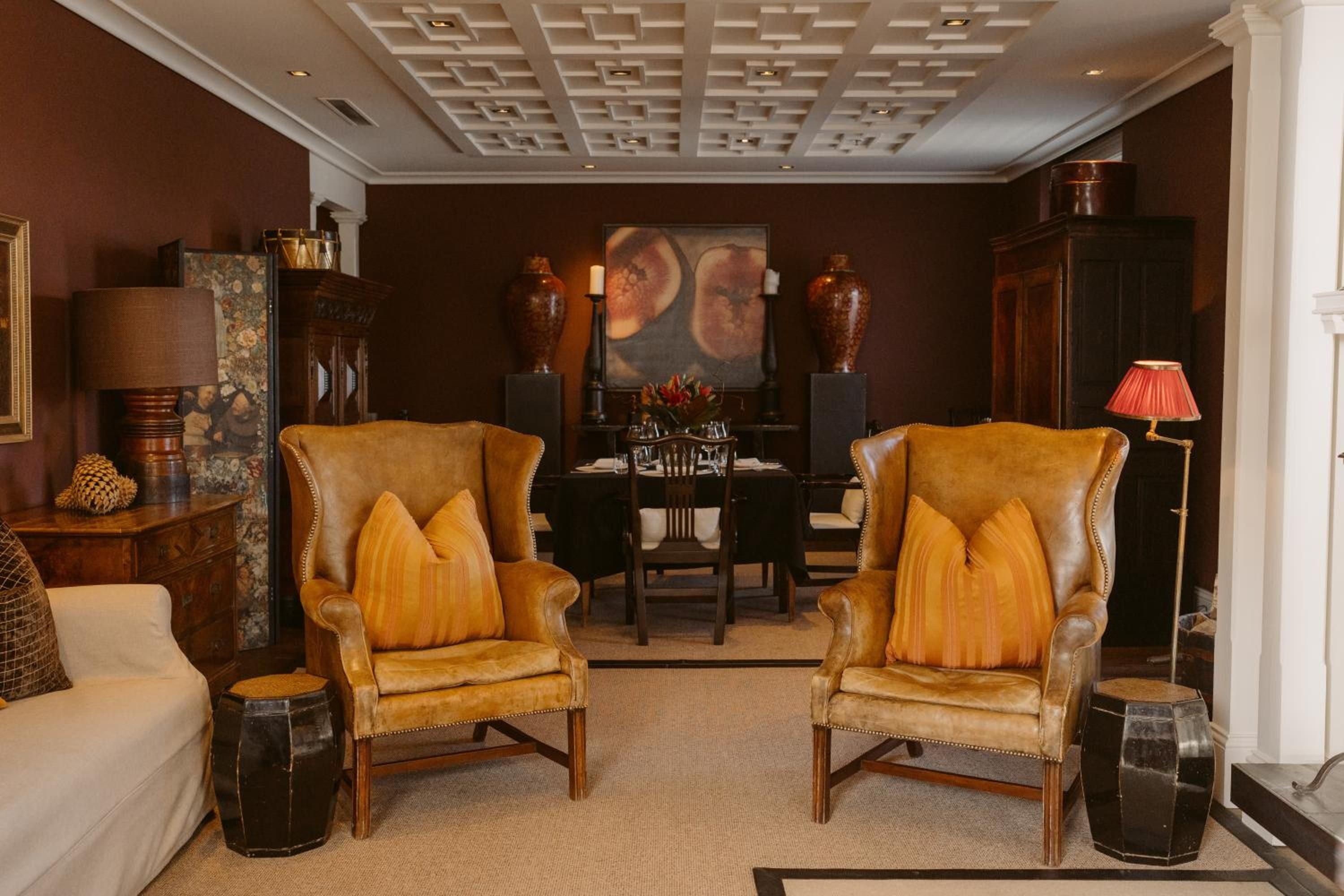 Rich cognac leather wingback chairs anchor an intimate seating area where warm amber light pools beneath an ornate coffered ceiling, creating sophisticated sanctuary.
