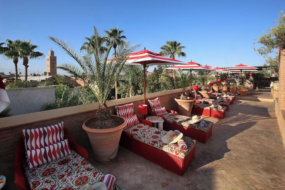 Red-striped umbrellas shade low-slung banquettes scattered across El Fenn's sun-baked rooftop terrace, where traditional textiles meet panoramic views of Marrakech's ancient medina.
