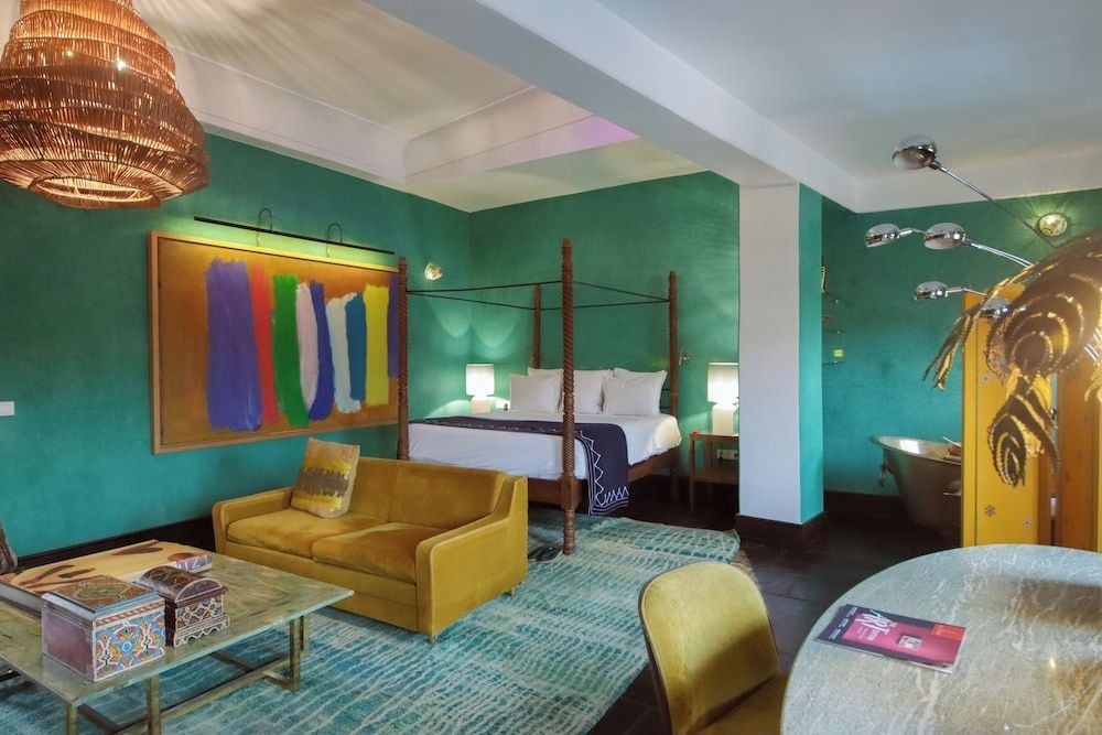 Vibrant turquoise walls frame a four-poster bed while golden velvet seating and woven pendant lighting create an intoxicating blend of Moroccan tradition and contemporary flair.