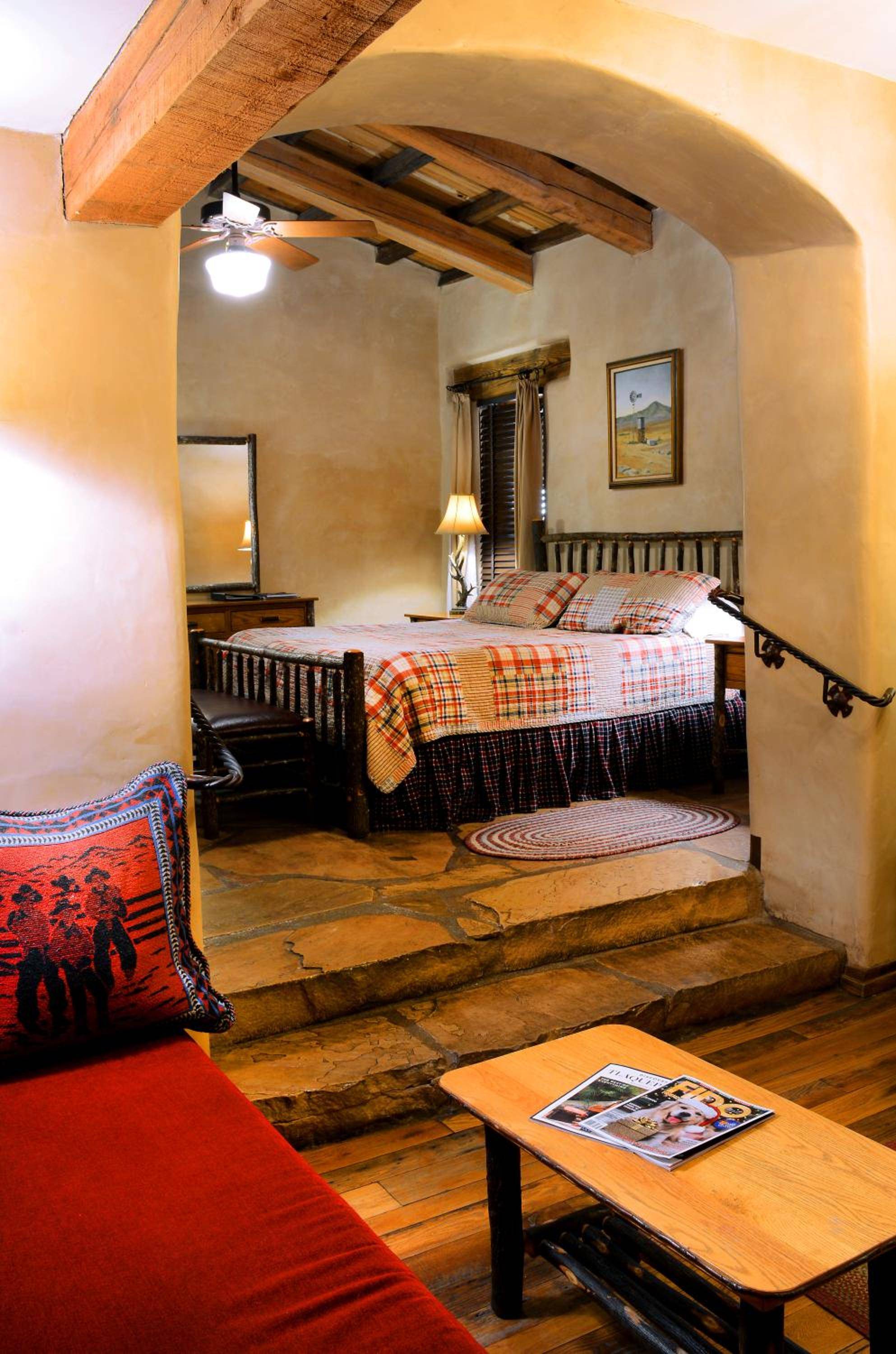 Rustic vigas frame an elevated sleeping alcove where plaid linens and Native American textiles create intimate warmth beneath honey-colored adobe arches.