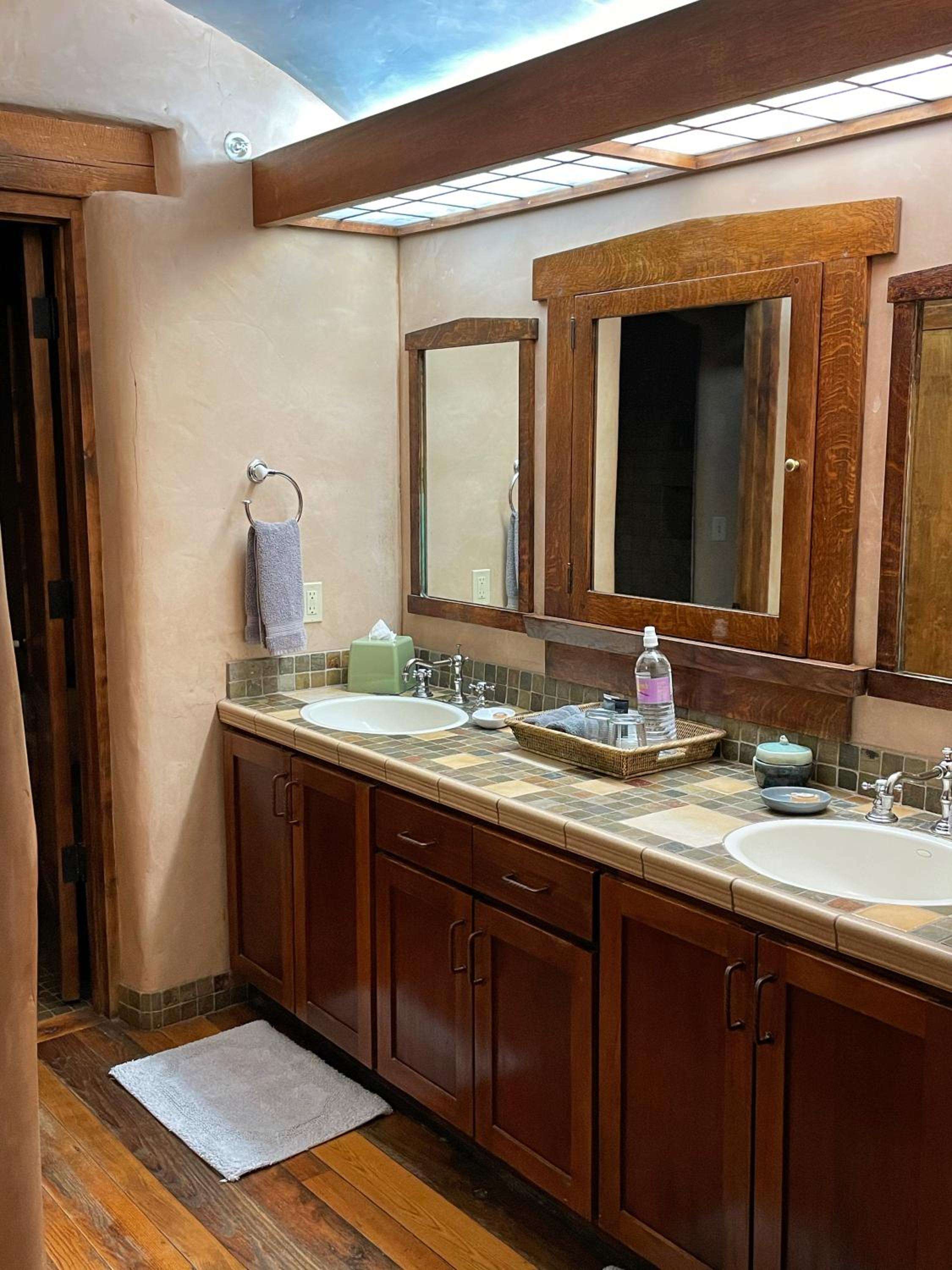 Rich oak cabinetry and handcrafted tile countertops create a warm, craftsman-style vanity where natural light streams through frosted glass above.