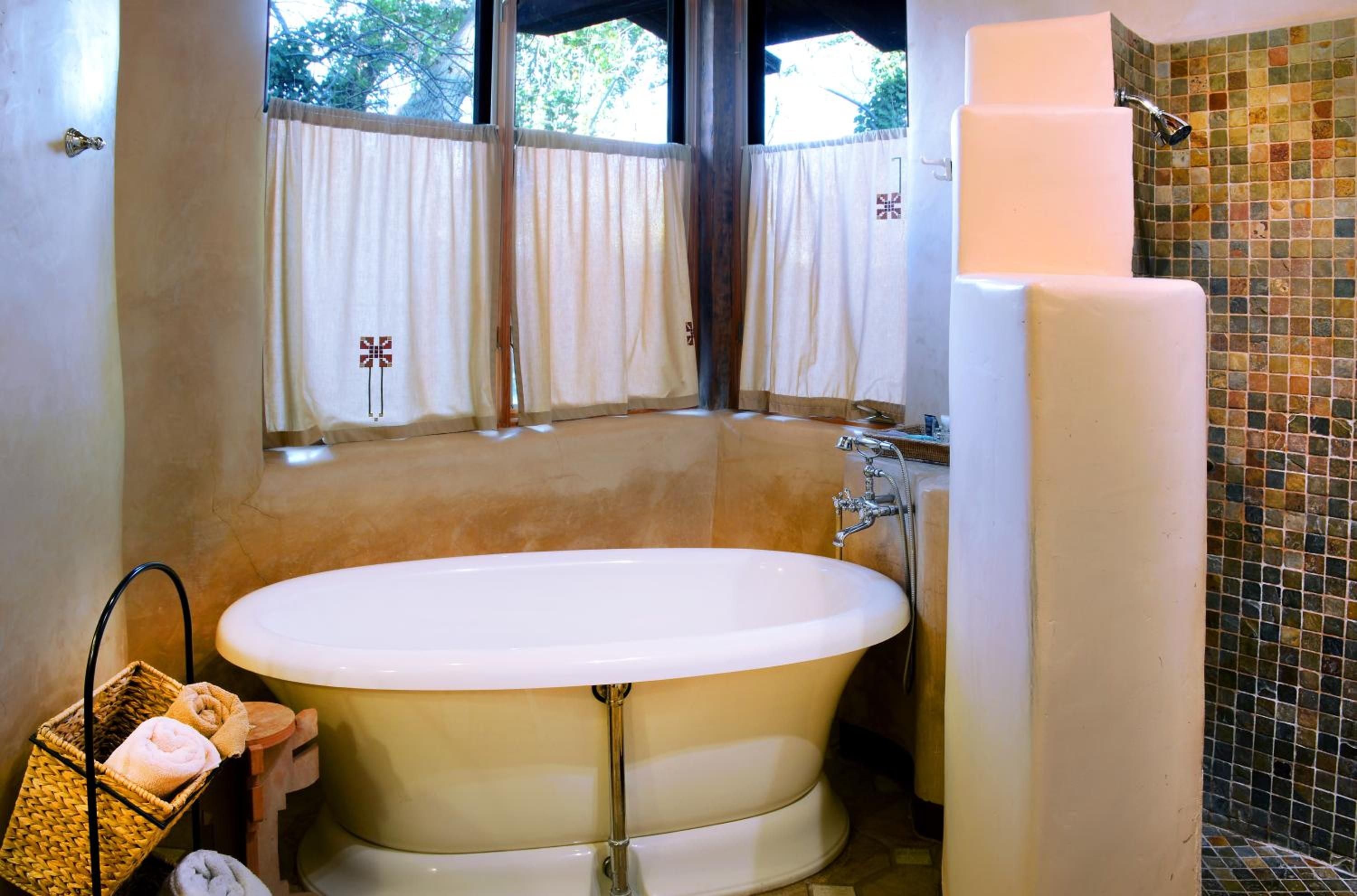 Golden afternoon light filters through café curtains onto a sculptural soaking tub, where mosaic tiles and polished concrete create an intimate sanctuary.