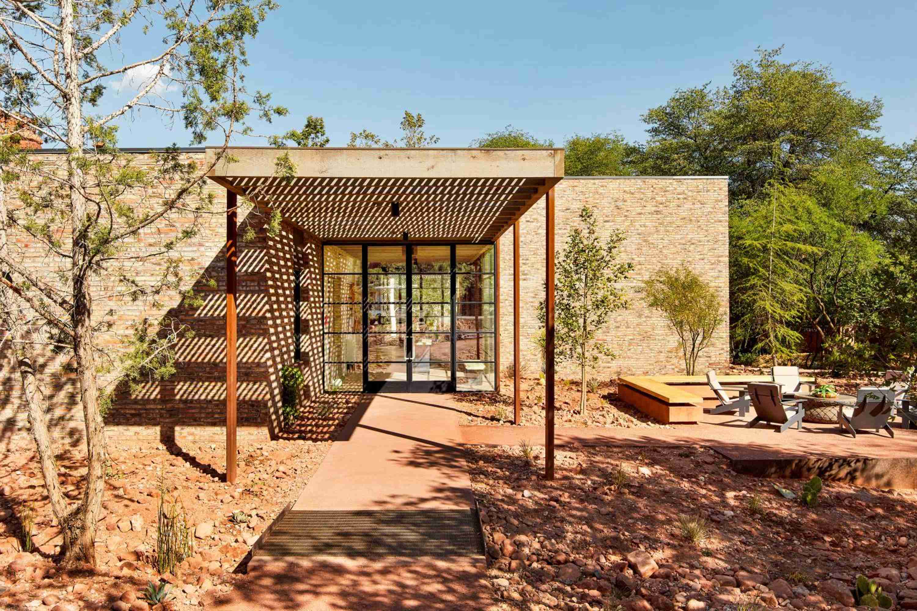 Desert-hued stone walls and geometric wooden lattework create striking interplay of light and shadow at this contemporary desert sanctuary nestled among ancient red rocks.
