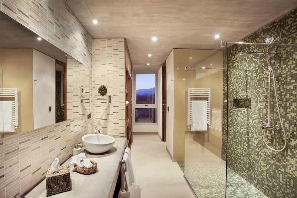 Stone mosaics and sleek fixtures create a spa-like sanctuary where rainfall showers and mountain views through glass doors elevate the daily ritual.
