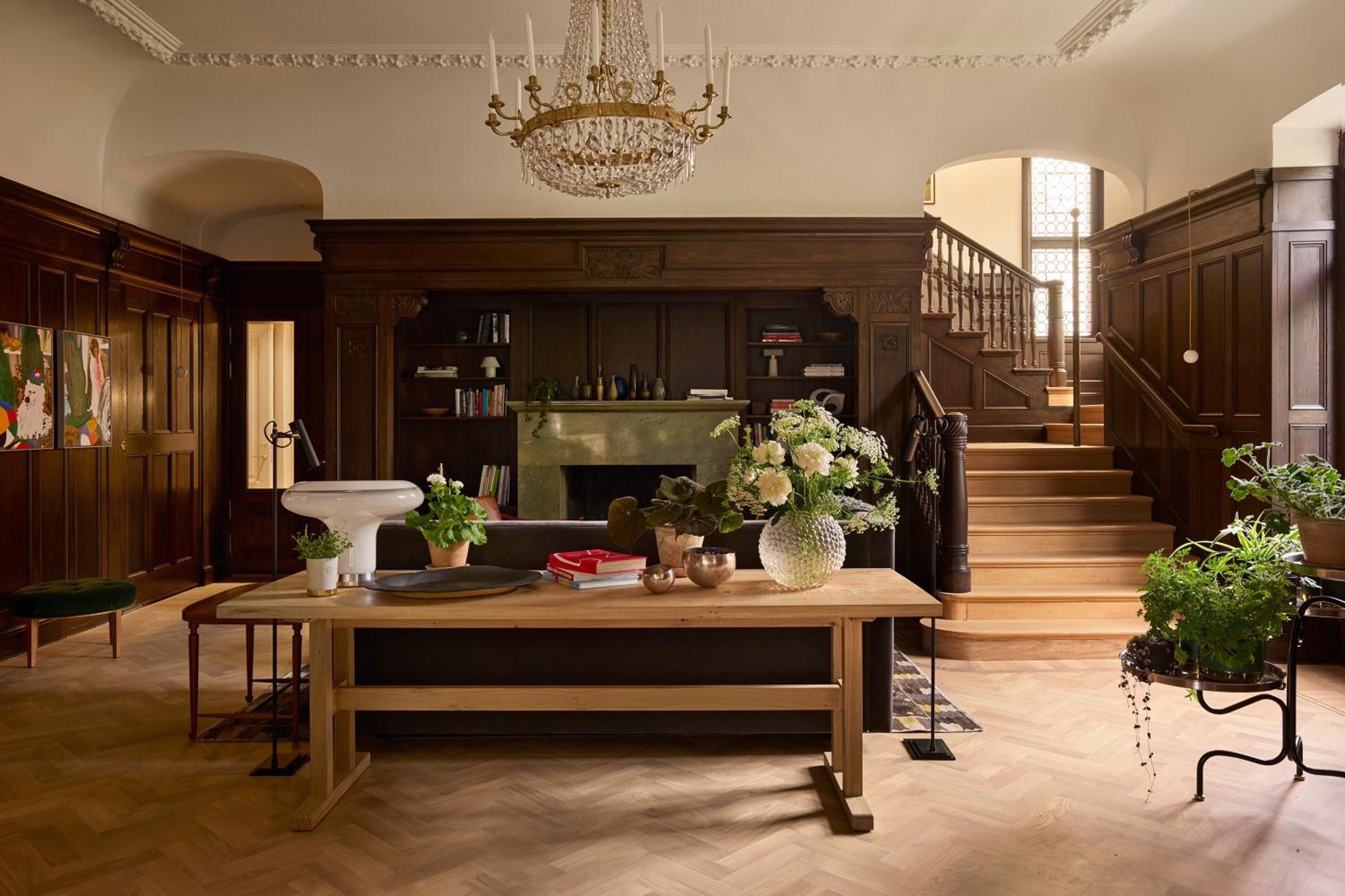 Rich walnut paneling and herringbone floors create an inviting living room where crystal chandeliers cast warm light over fresh blooms and well-worn leather chairs.