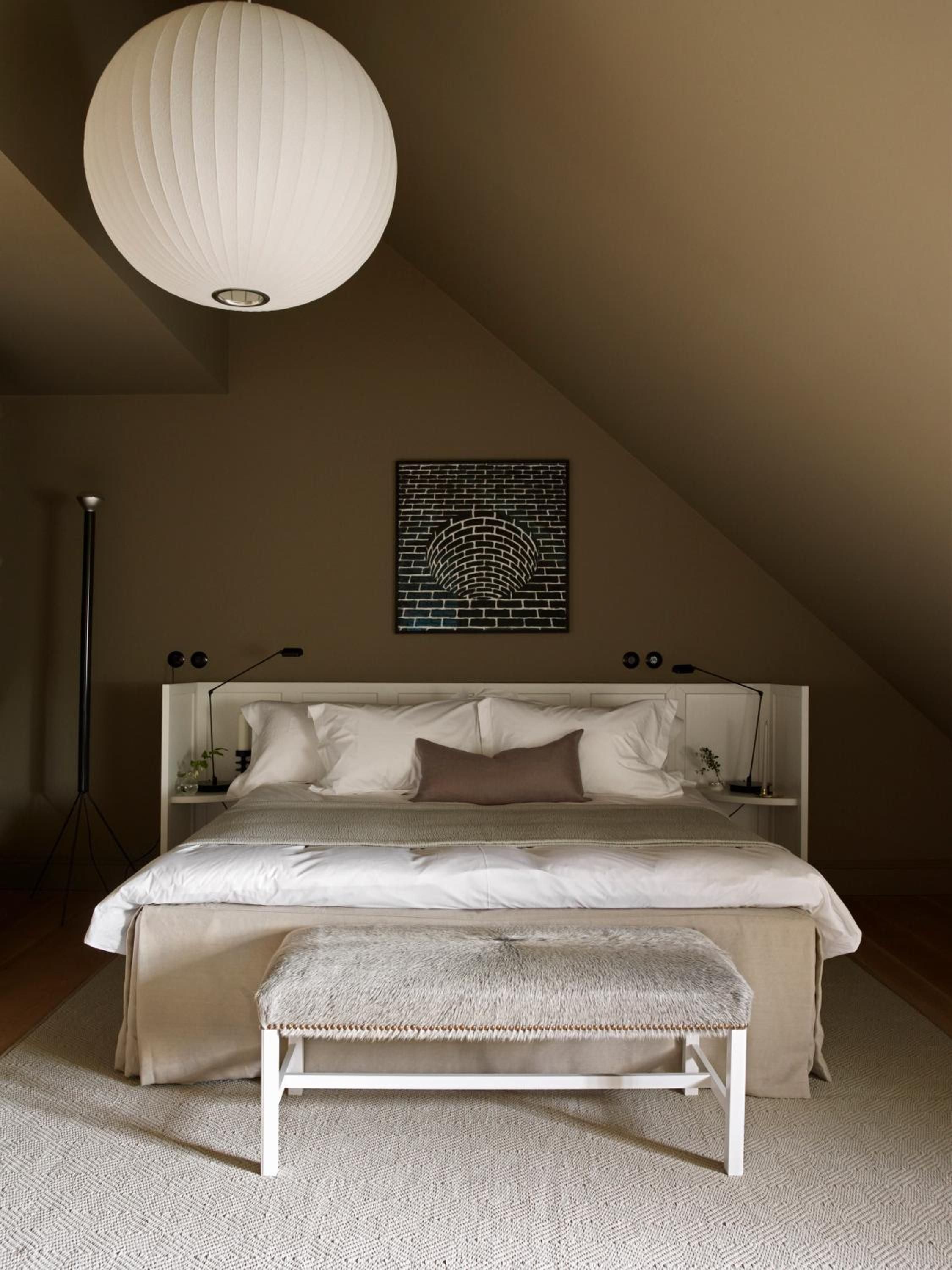 Soft linen bedding and ribbed pendant lighting create intimate warmth in this attic sanctuary, where brick archway art anchors the sloped ceiling's cozy embrace.