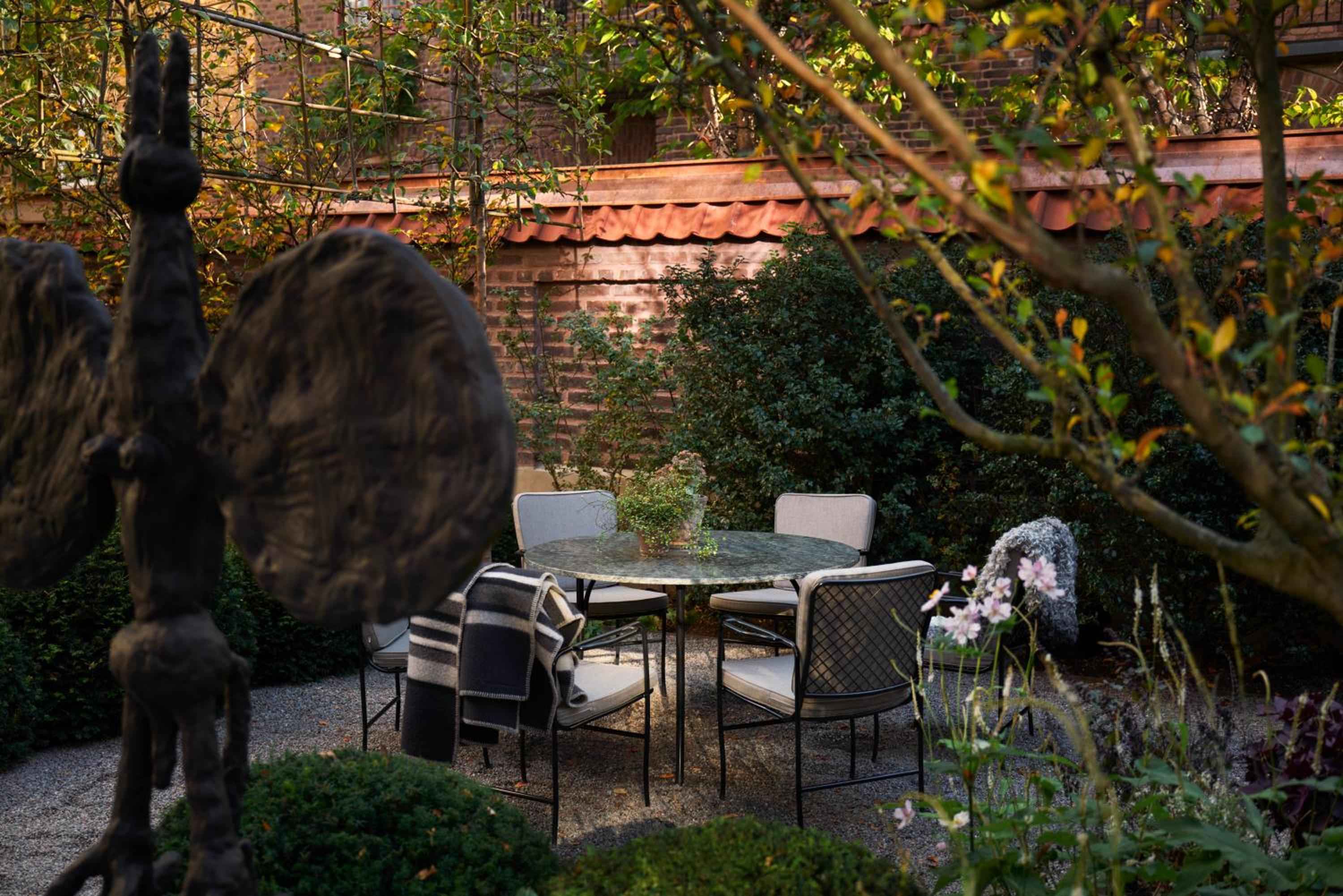 Dappled autumn light filters through bare branches onto intimate garden seating, where weathered brick walls and sculptural elements create a secret Stockholm sanctuary.