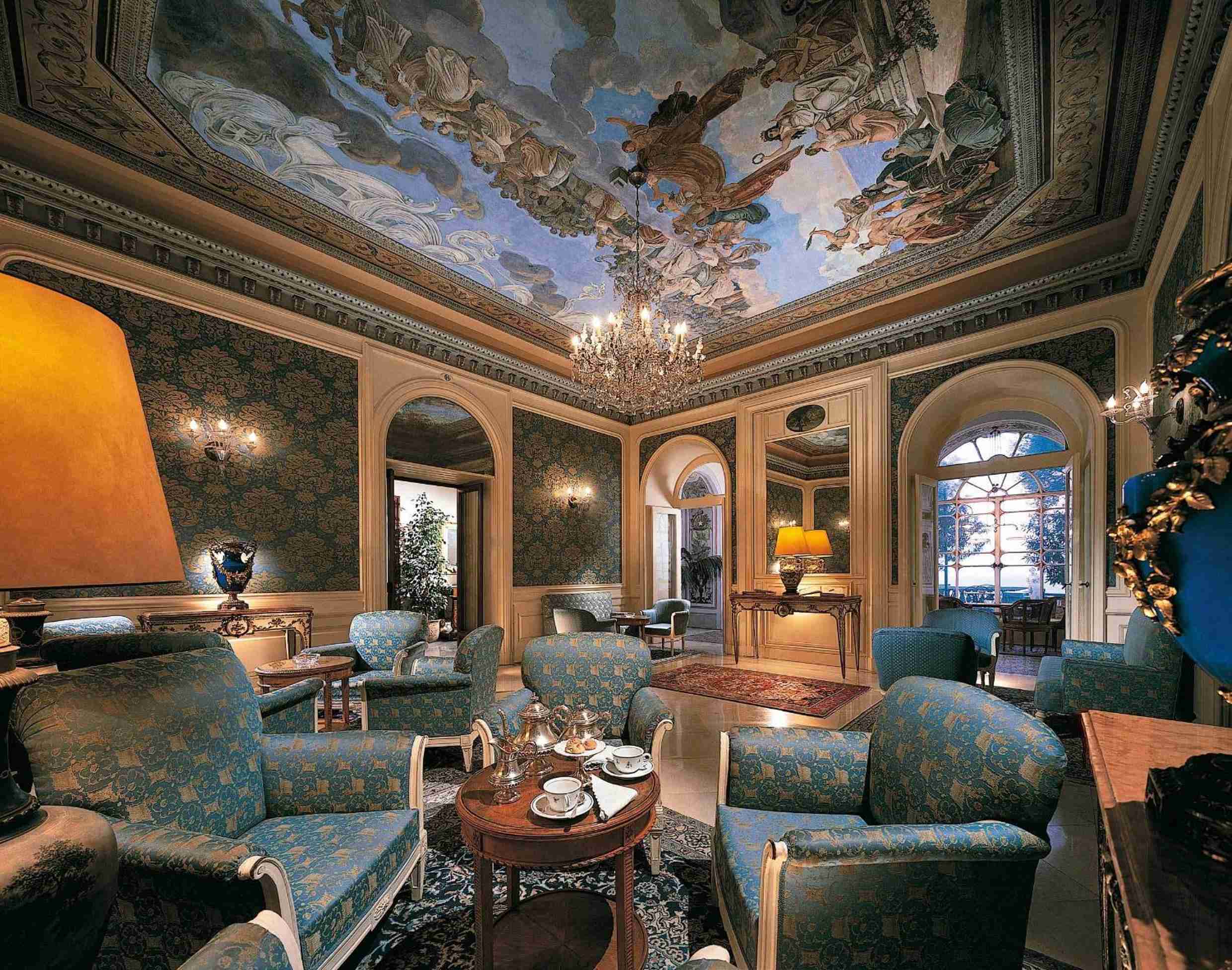 Baroque grandeur meets intimate luxury in this palatial salon, where hand-painted celestial frescoes soar above sumptuous blue brocade seating and gleaming crystal chandeliers.
