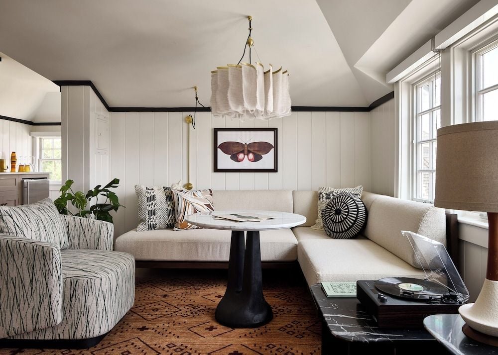 Nautical charm meets modern comfort in this inviting nook, where geometric pillows and a striking moth print create conversation corners beneath natural linen chandeliers.
