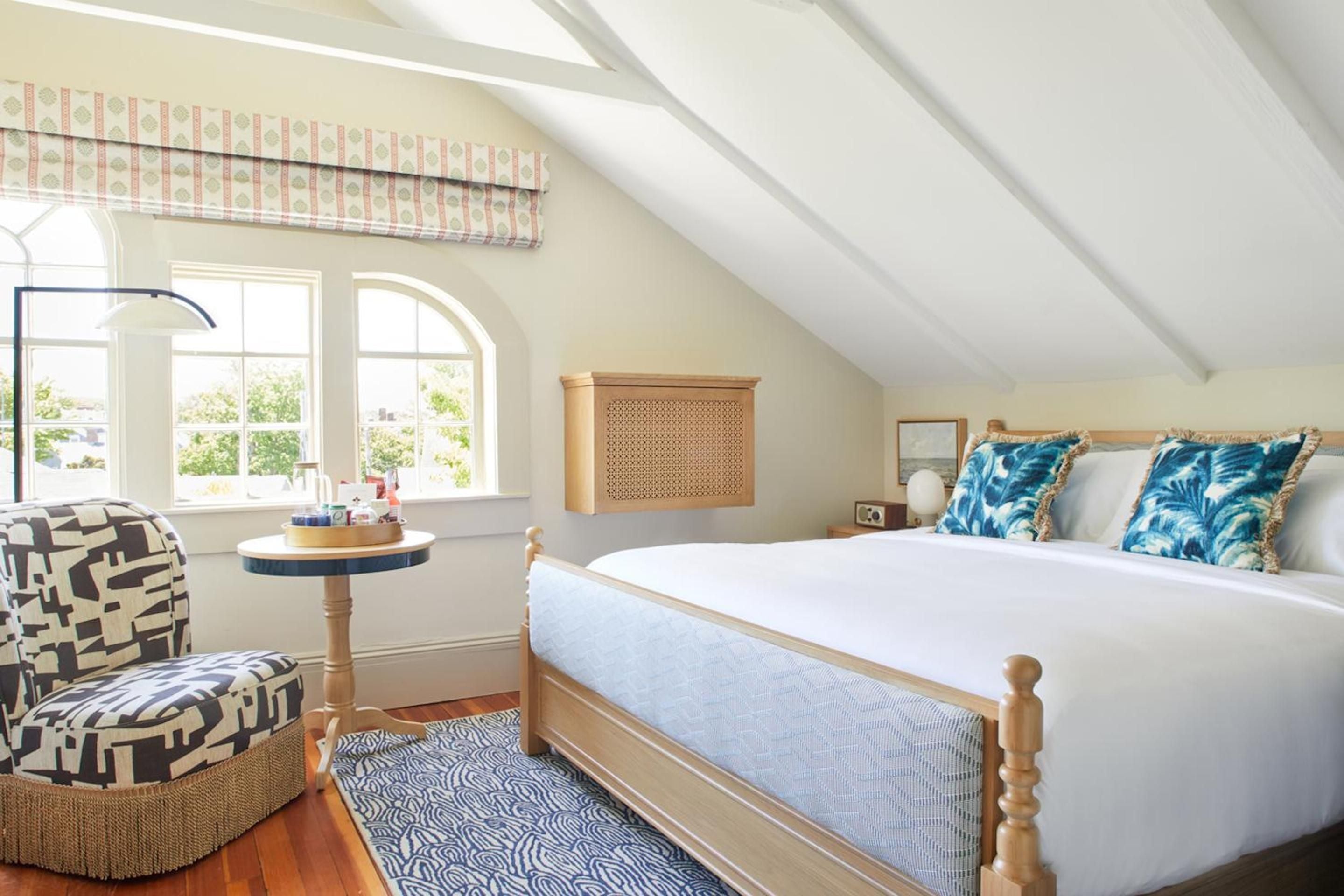 Rope-trimmed pillows and weathered wood beams create coastal charm in this attic sanctuary, where morning light streams through arched windows onto blue-striped rugs.