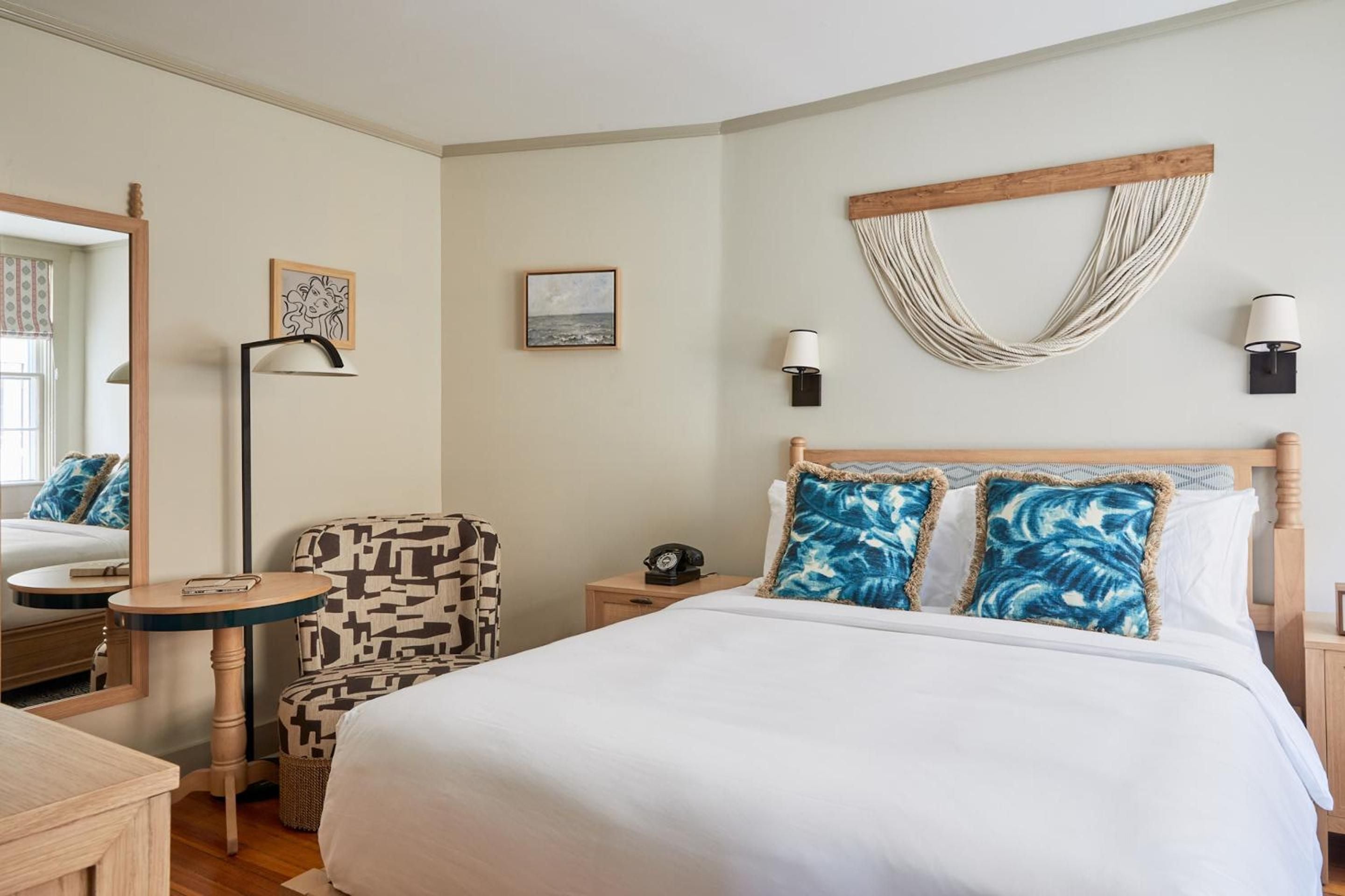 Natural rope art and vibrant blue pillows create coastal charm in this thoughtfully appointed guest room, where warm wood tones meet crisp white linens.