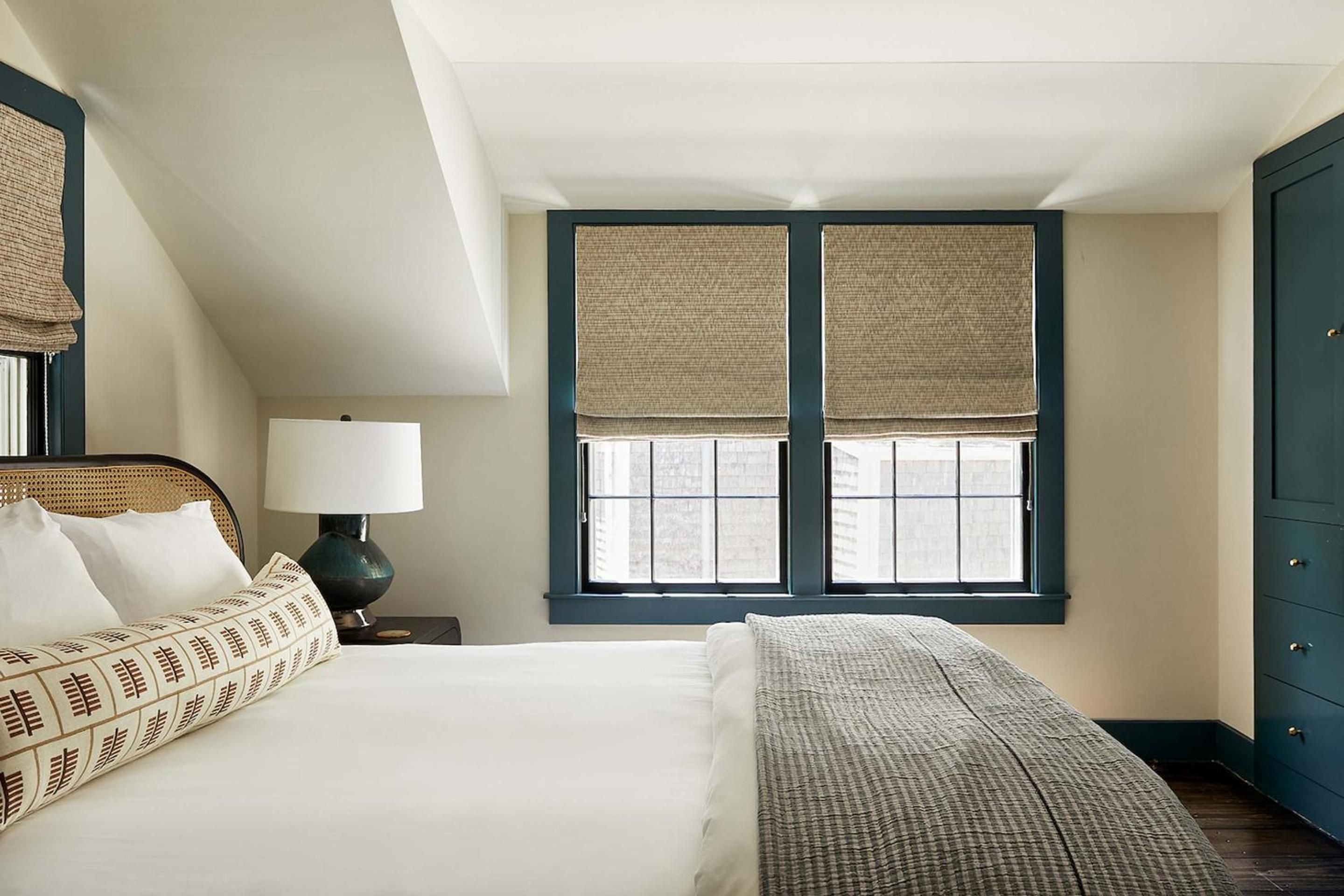 Woven rattan headboards and sage-green built-ins create coastal sophistication in guest rooms, where natural textures meet crisp white linens and thoughtful nautical touches.