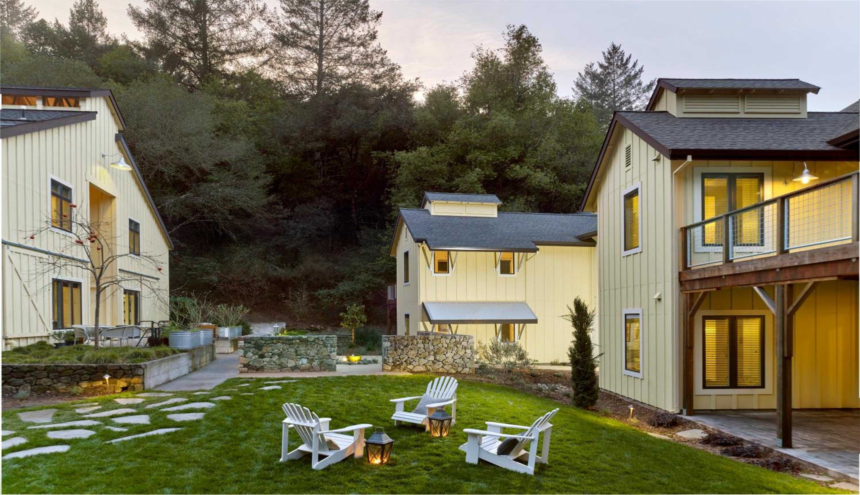 Cream-colored cottages nestle into wooded hillsides while Adirondack chairs circle the central lawn, creating an intimate village feel at dusk.