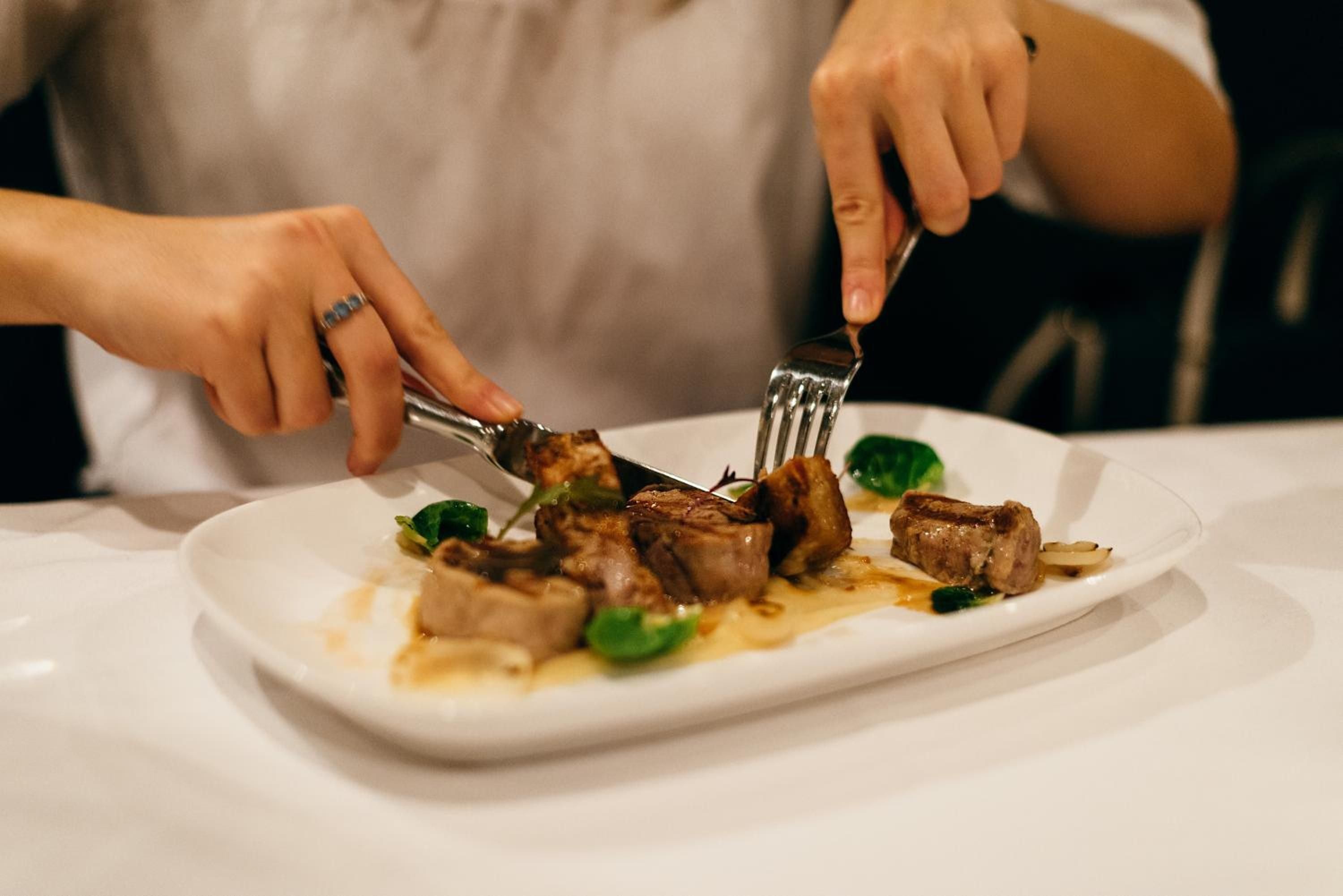 Hands expertly slice into perfectly seared meat at Farmhouse Inn's acclaimed restaurant, where each dish showcases Sonoma County's finest ingredients with refined, rustic elegance.