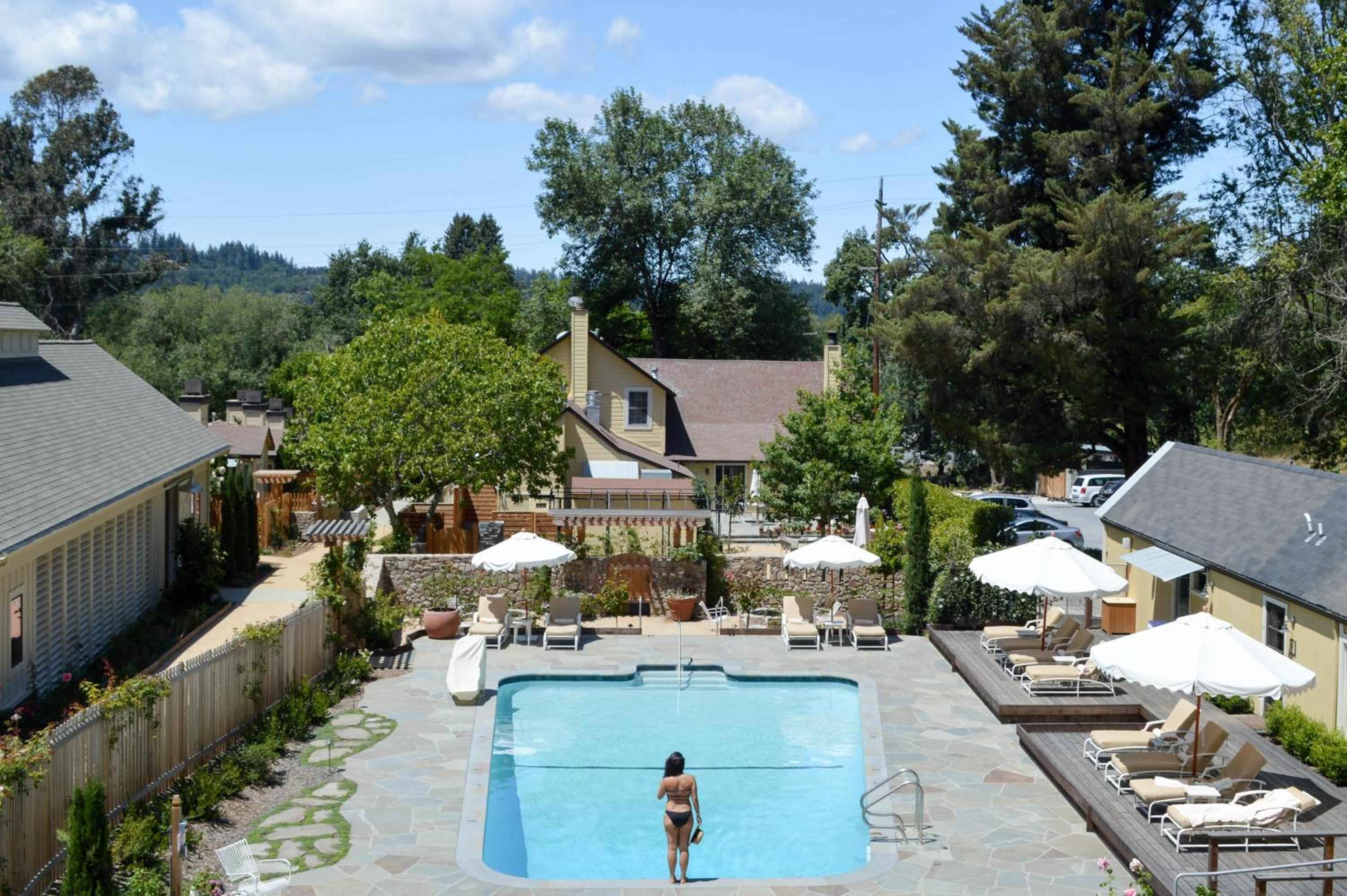 Sun-dappled stone decking surrounds the pristine pool, where white umbrellas cast gentle shadows and rolling Sonoma hills provide a serene backdrop for afternoon swims.