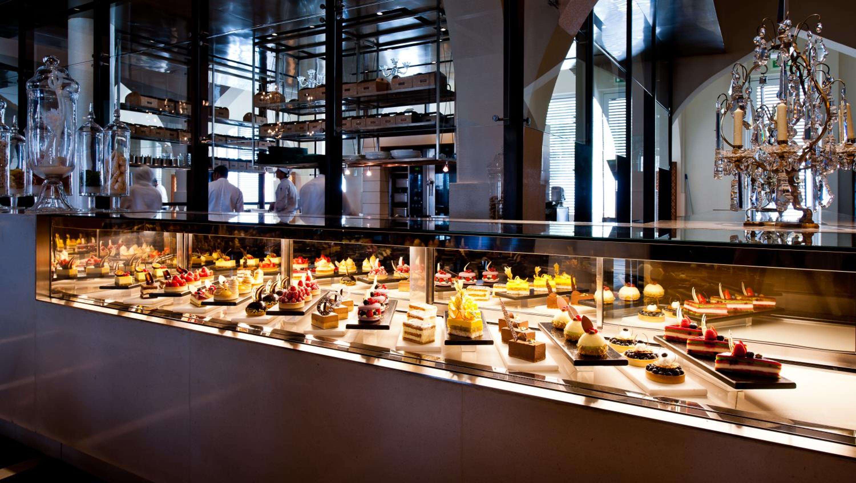 Artfully arranged pastries and desserts gleam under warm lighting in this sophisticated patisserie display, where culinary craftsmanship meets elegant presentation behind pristine glass cases.