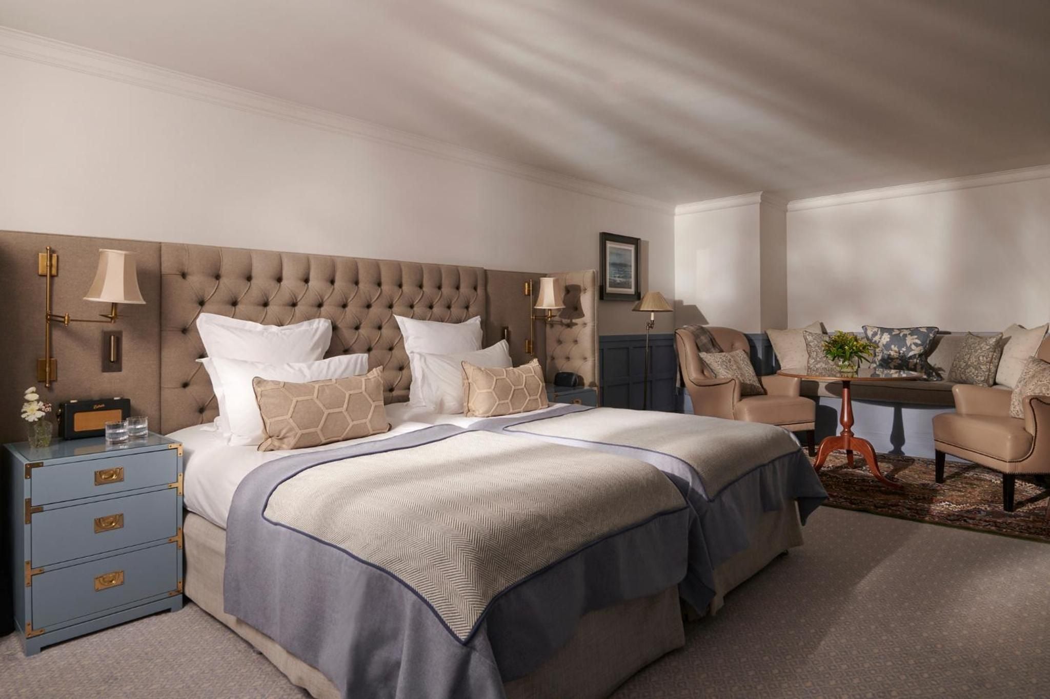 Tufted taupe headboards and brass campaign furniture create an elegant retreat where slanted ceilings add intimate charm to this sophisticated Highland sanctuary.