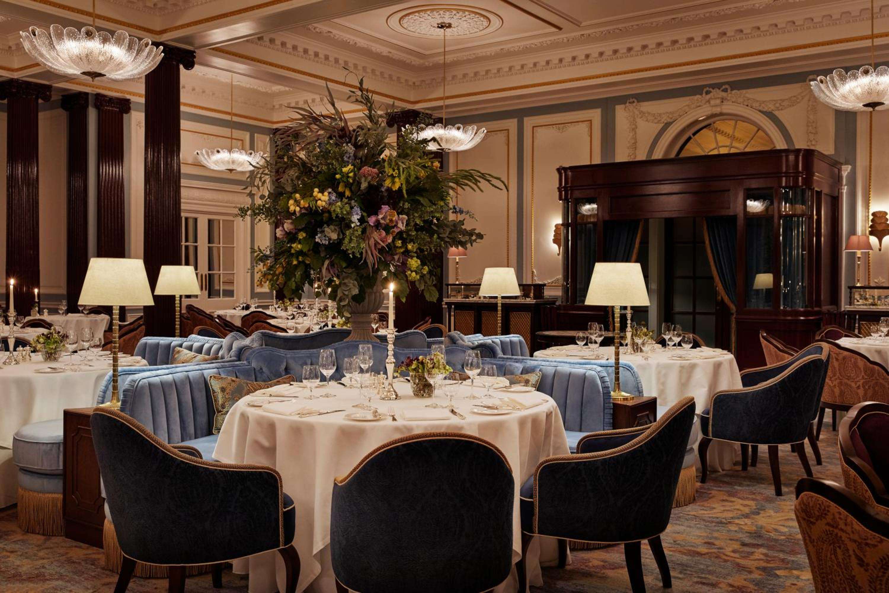 Crystal chandeliers cast warm light over intimate tables where crisp linens meet navy velvet banquettes, creating an atmosphere of refined Scottish elegance.