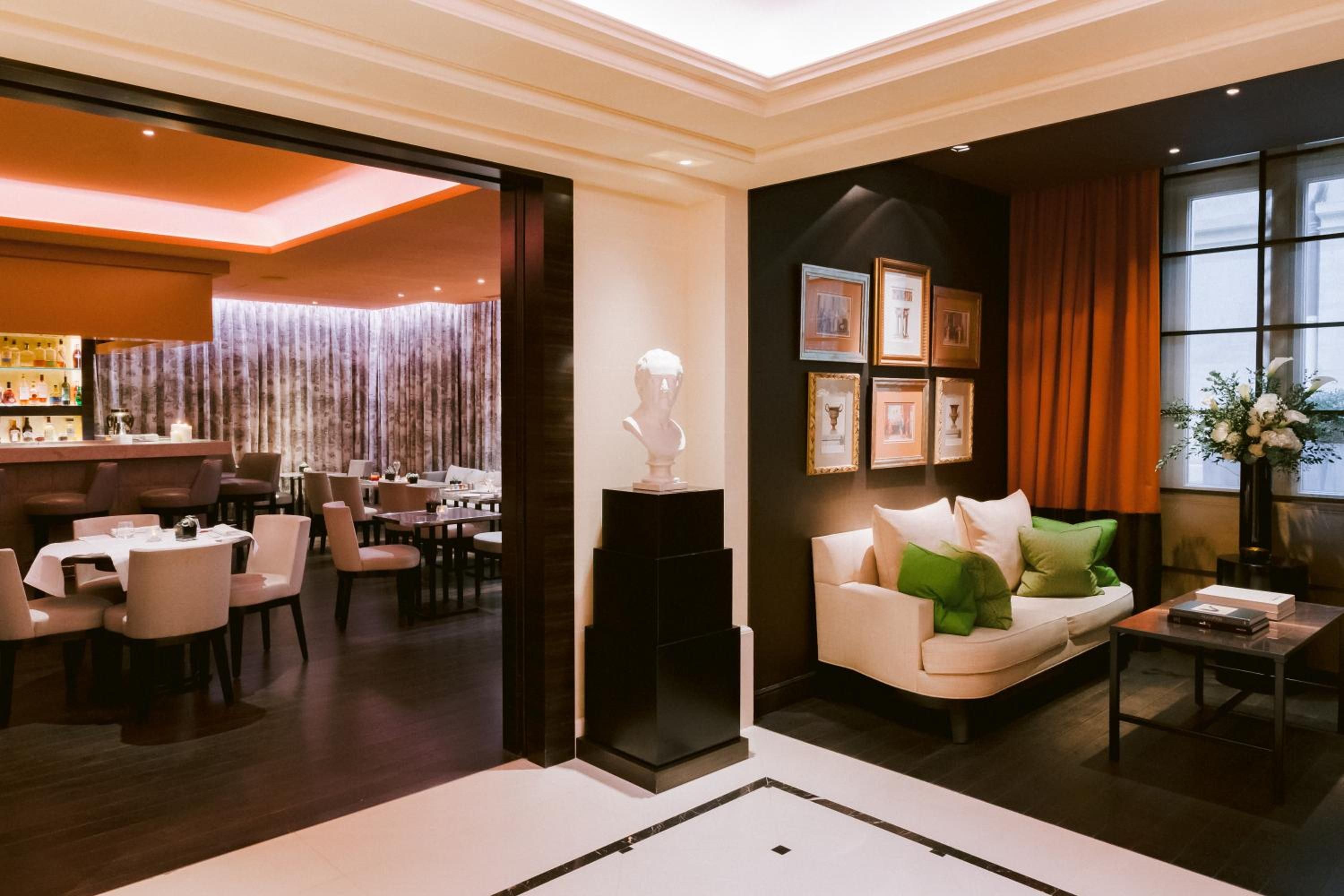 Warm amber lighting and rich mahogany frames create an intimate lounge where classical busts watch over plush seating before the elegant dining room beckons.