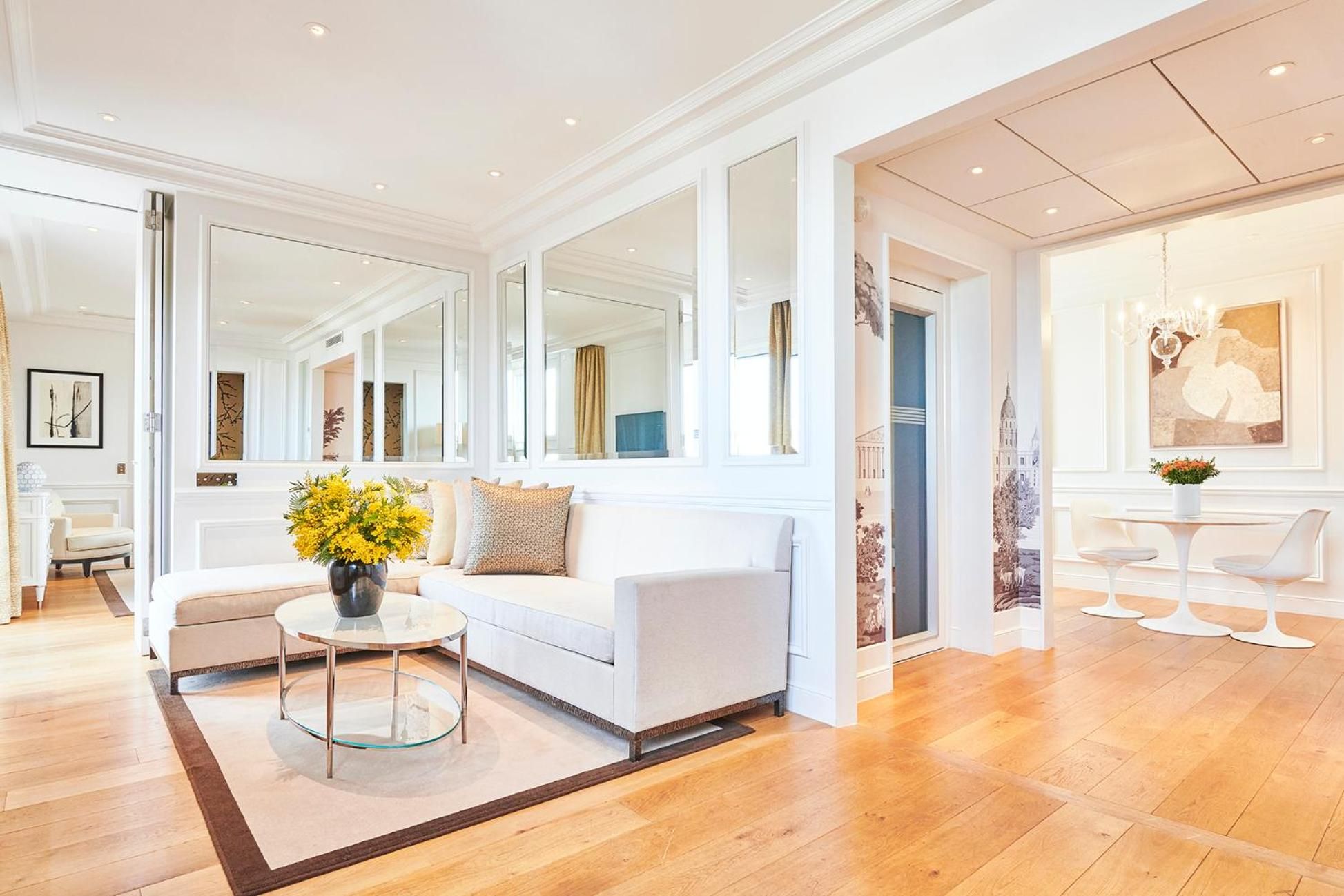 Mirrored room dividers and honey-toned hardwood floors create an airy elegance in this Parisian suite, where golden sunflowers echo the warm light streaming through tall windows.
