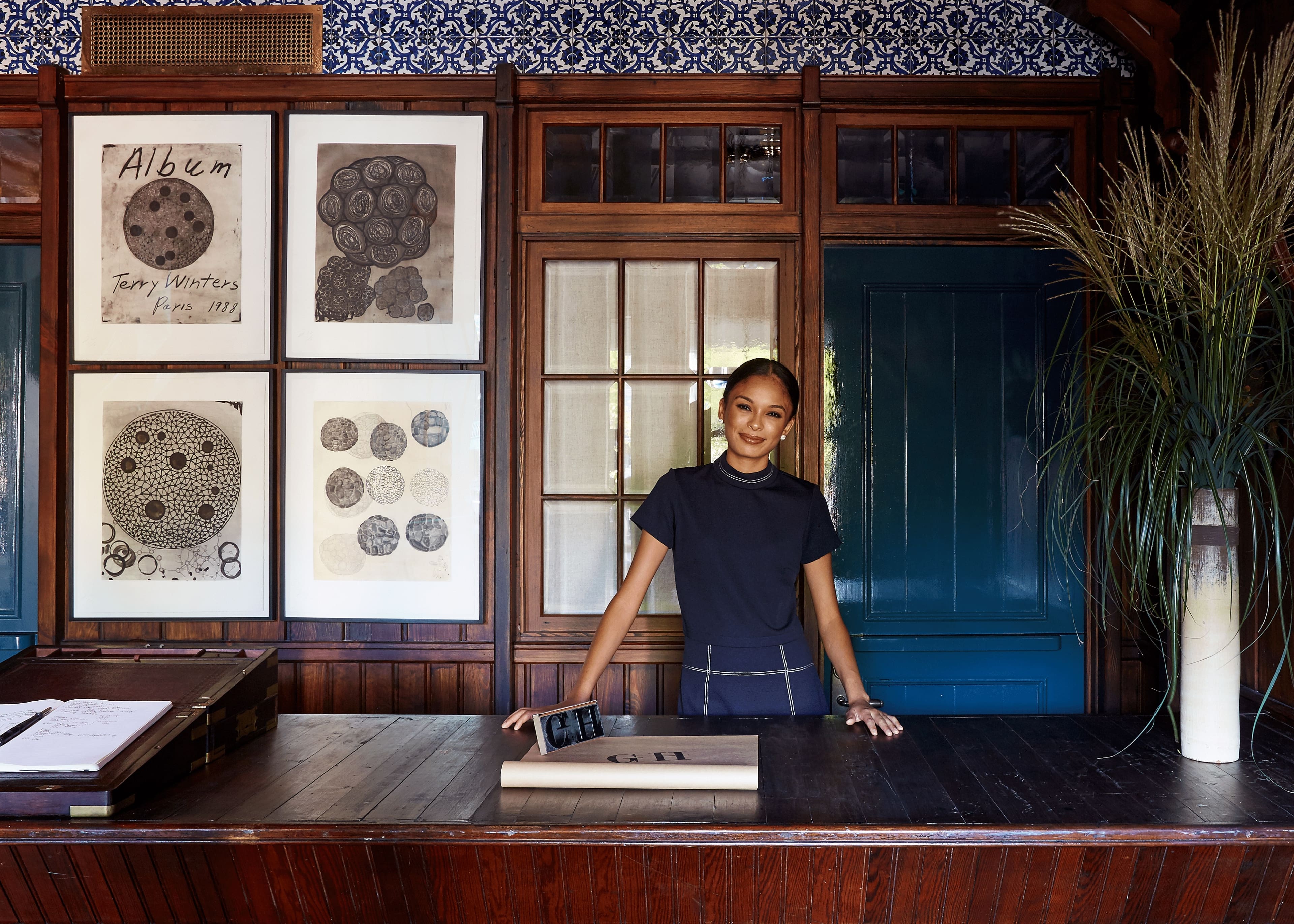 Vintage botanical prints and patterned wallpaper create an intimate backdrop at the reception desk, where warm wood tones meet navy accents in this thoughtfully curated space.