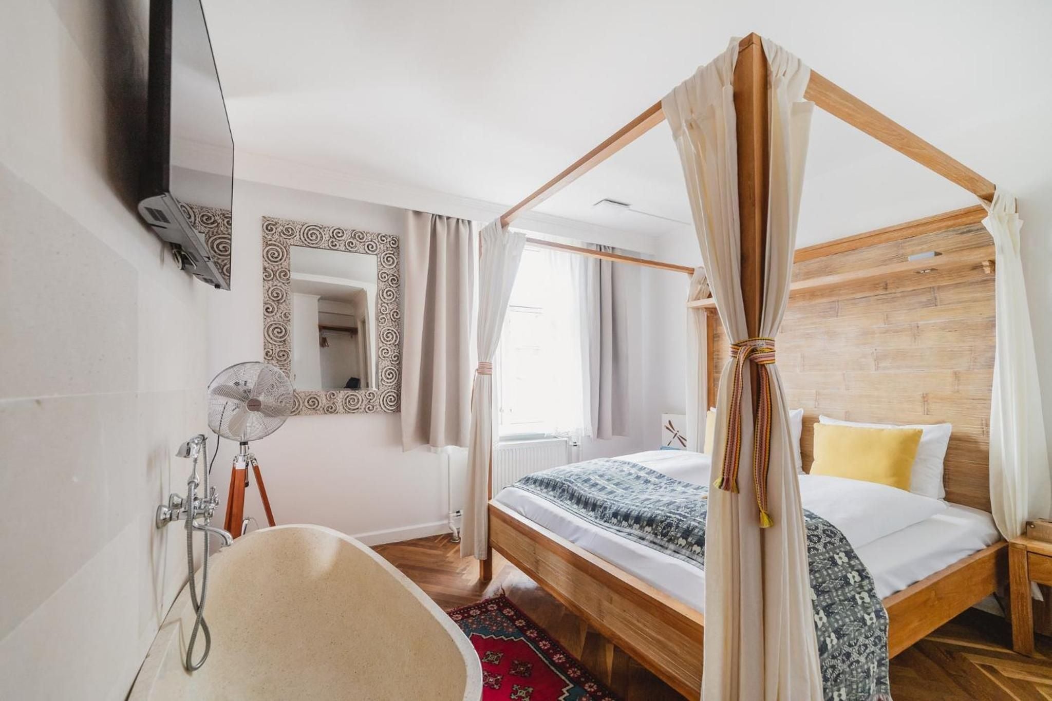 Natural linen drapes frame the handcrafted four-poster bed, while warm wood tones and vintage Persian rugs create an intimate bohemian sanctuary.