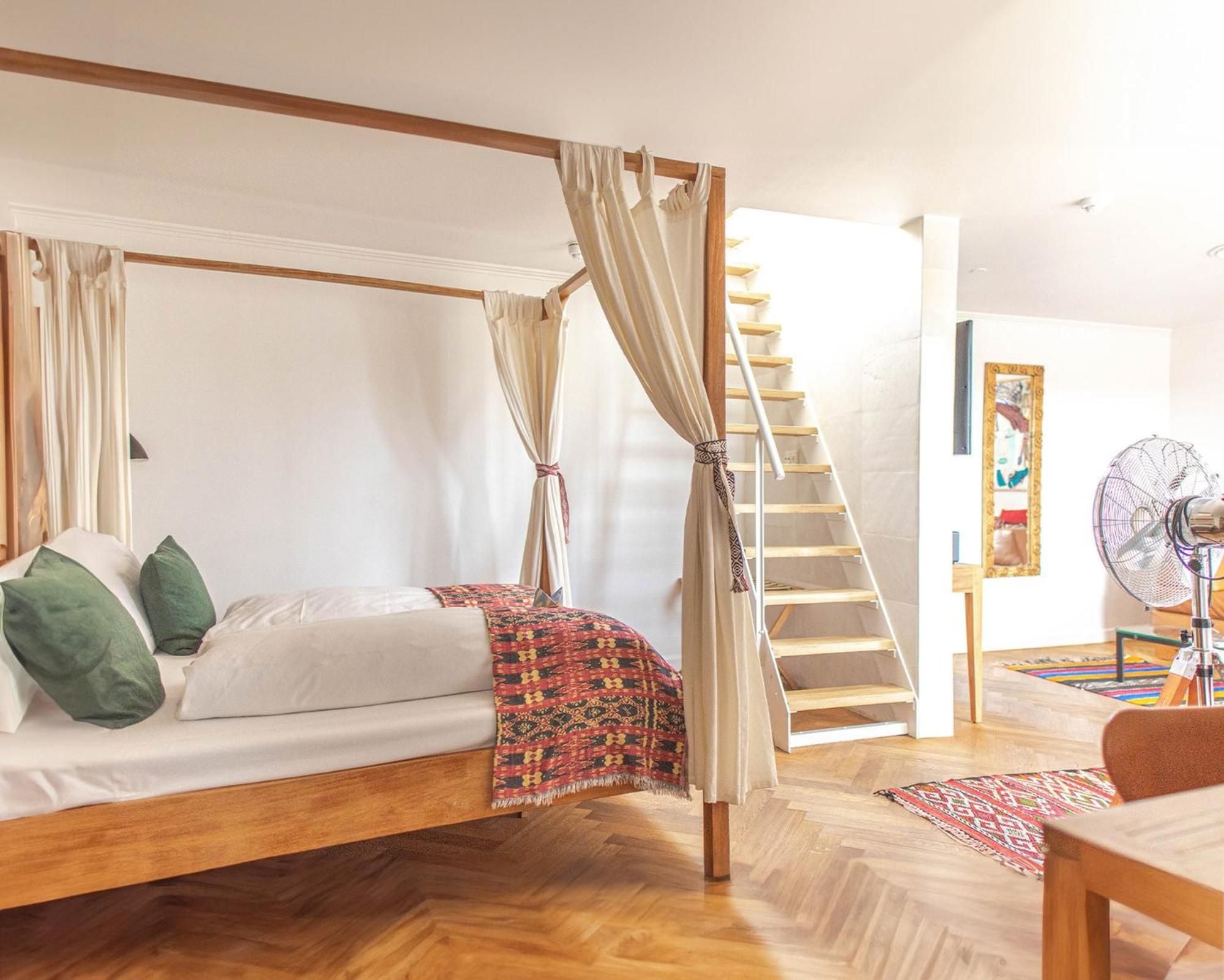 Natural linen curtains frame the four-poster bed while warm wood floors and tribal textiles create an inviting bohemian sanctuary beneath soaring ceilings.