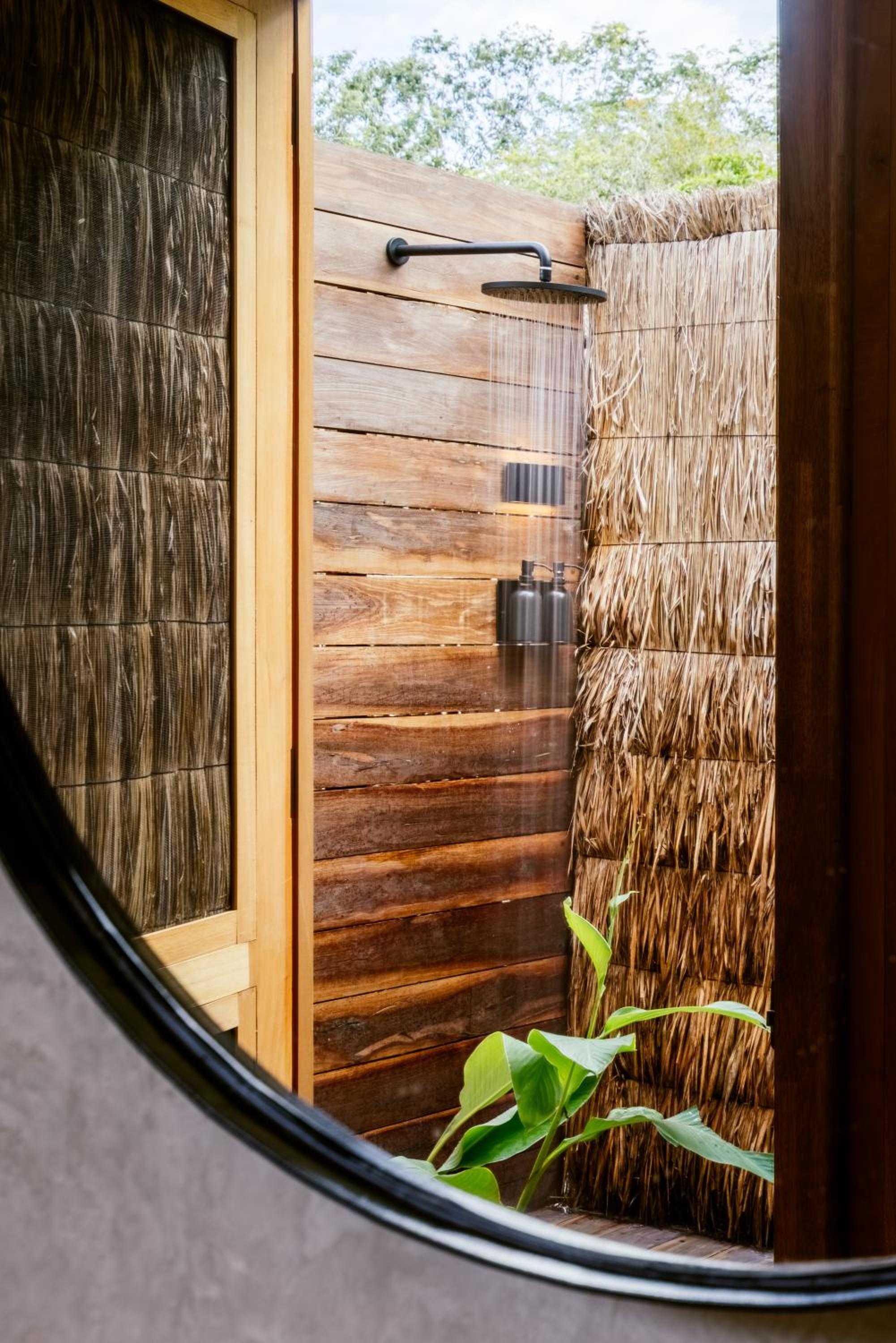 Natural materials create an open-air shower sanctuary where warm teak planks meet woven palm screens, blending seamlessly with Bacalar's jungle setting.