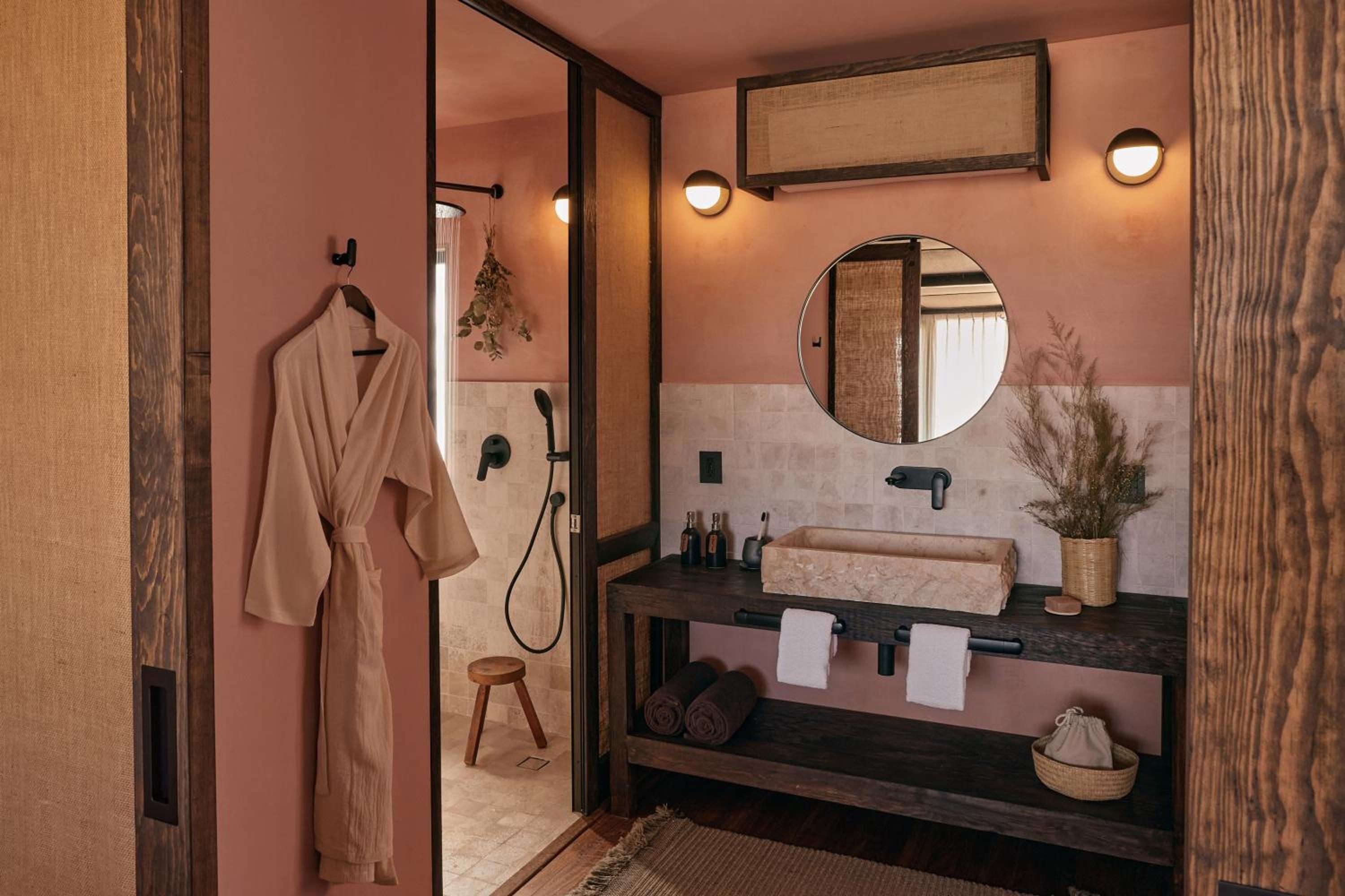 Warm terracotta walls frame sleek black fixtures and natural textures, where floating vanities and woven baskets create an earthy-luxe sanctuary with Japanese-inspired sensibilities.