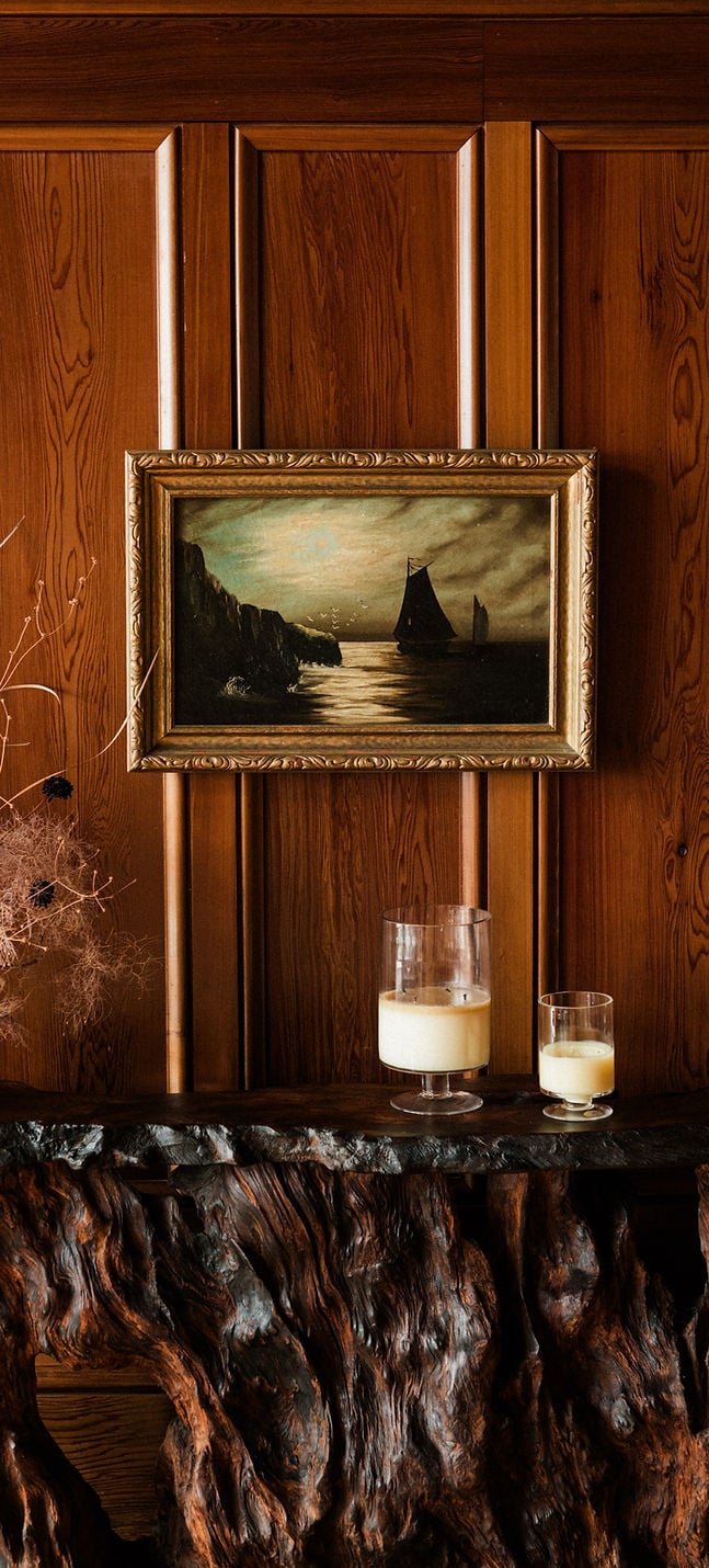 Maritime artwork and handcrafted cocktails find their place against rich wood paneling, where weathered driftwood shelving adds coastal character to intimate evening moments.