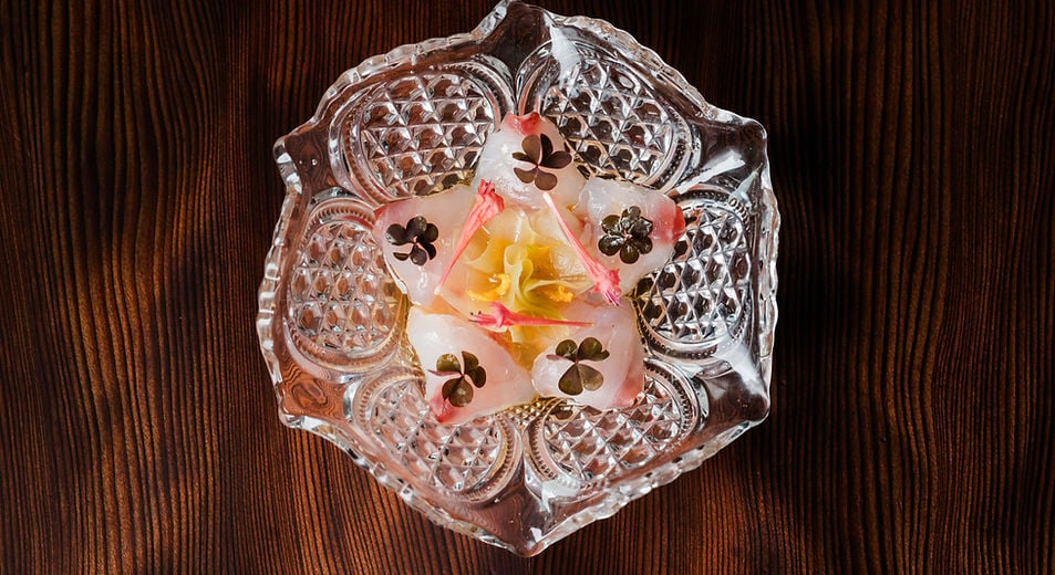 Delicate edible flowers float in crystalline ice within an ornate cut-glass bowl, showcasing Harbor House's meticulous attention to culinary artistry and presentation.