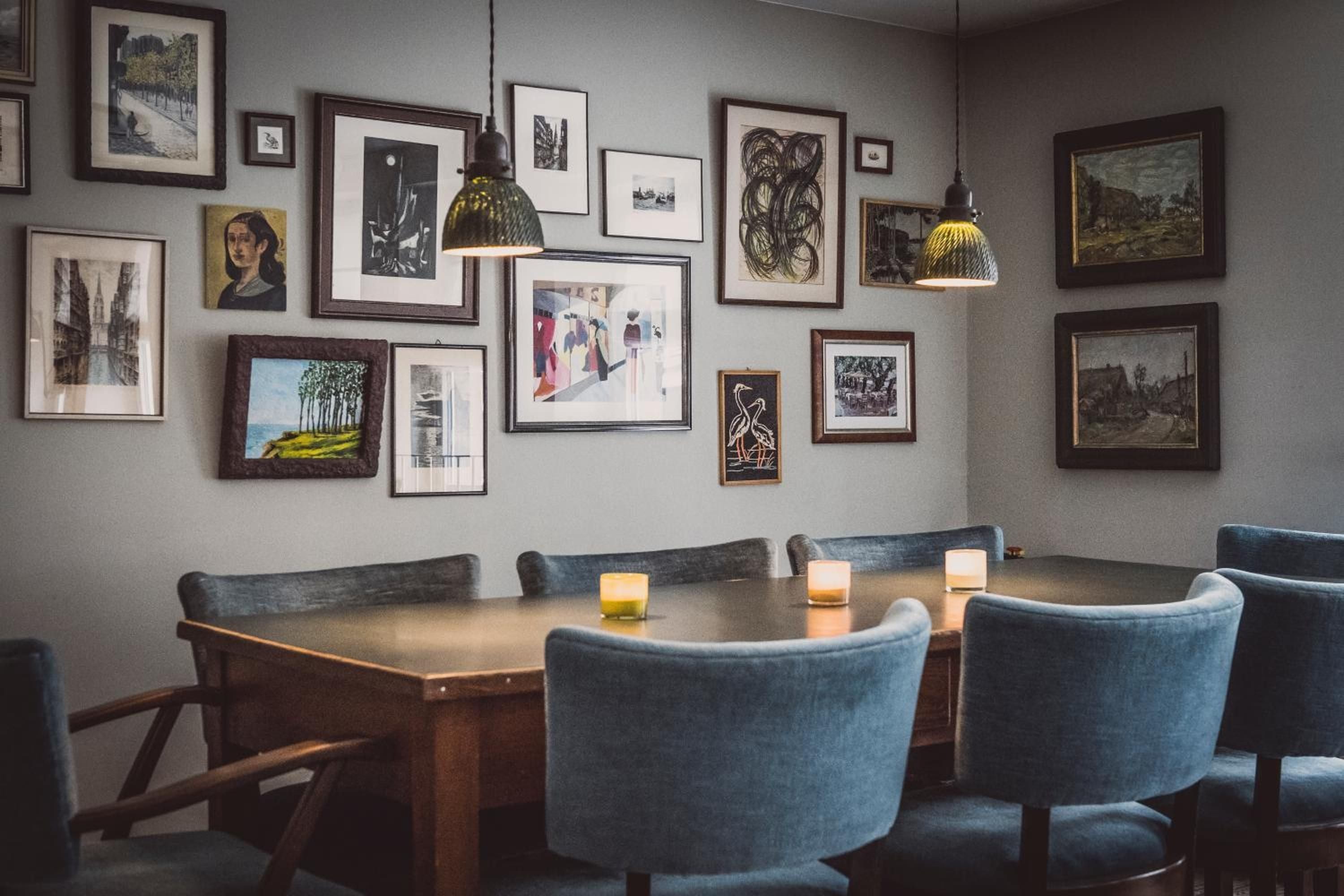 Thoughtfully curated artwork creates an intimate gallery atmosphere in the dining space, where flickering candles and rich blue velvet chairs invite lingering conversations over expertly crafted meals.