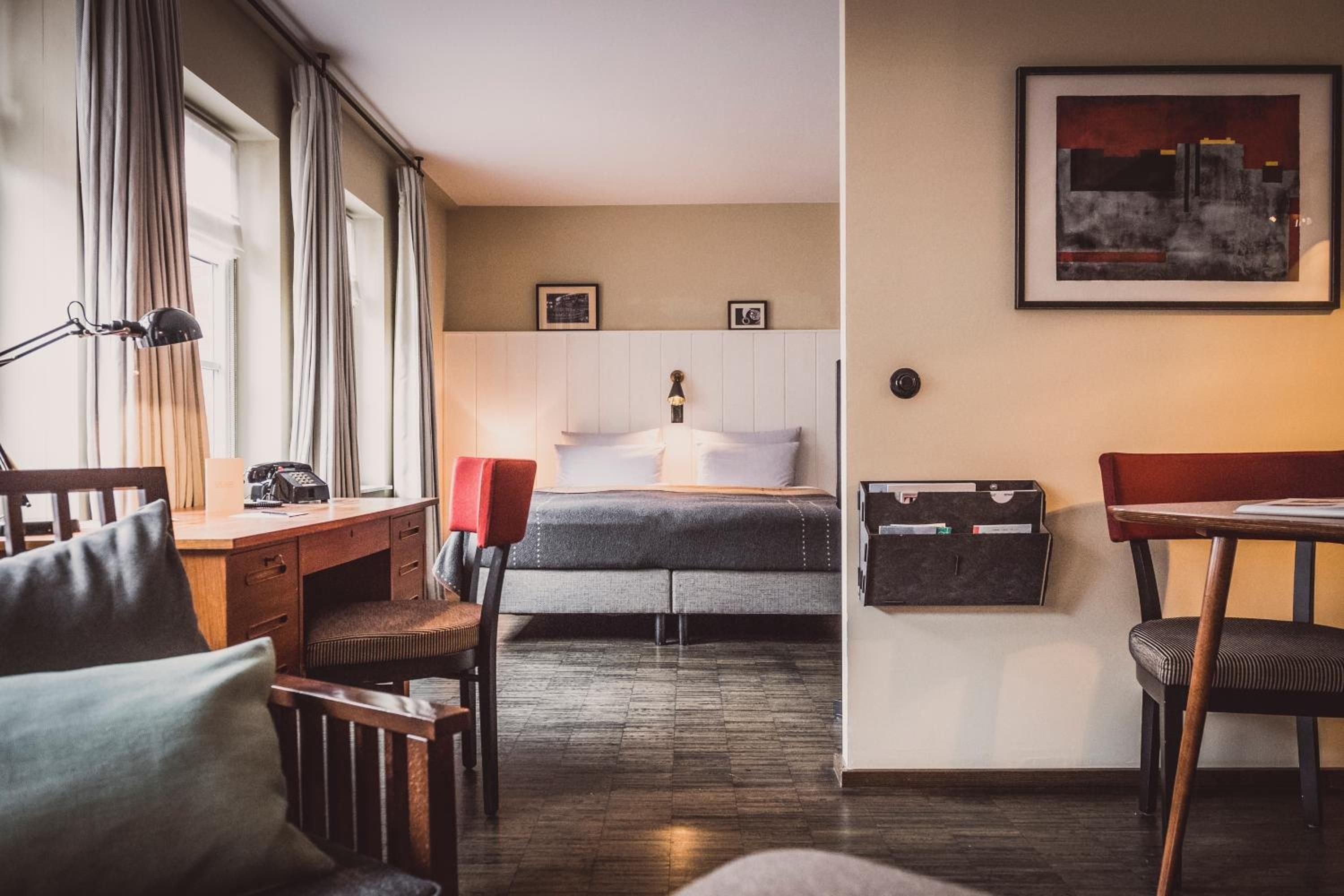 Mid-century walnut furniture and crisp white linens create a sophisticated sanctuary where warm afternoon light filters through floor-to-ceiling windows onto polished hardwood floors.
