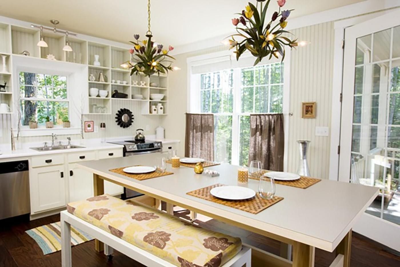 Sunlight streams through café curtains into this cottage-style kitchen where floral chandeliers bloom overhead and woven placemats await intimate family gatherings.