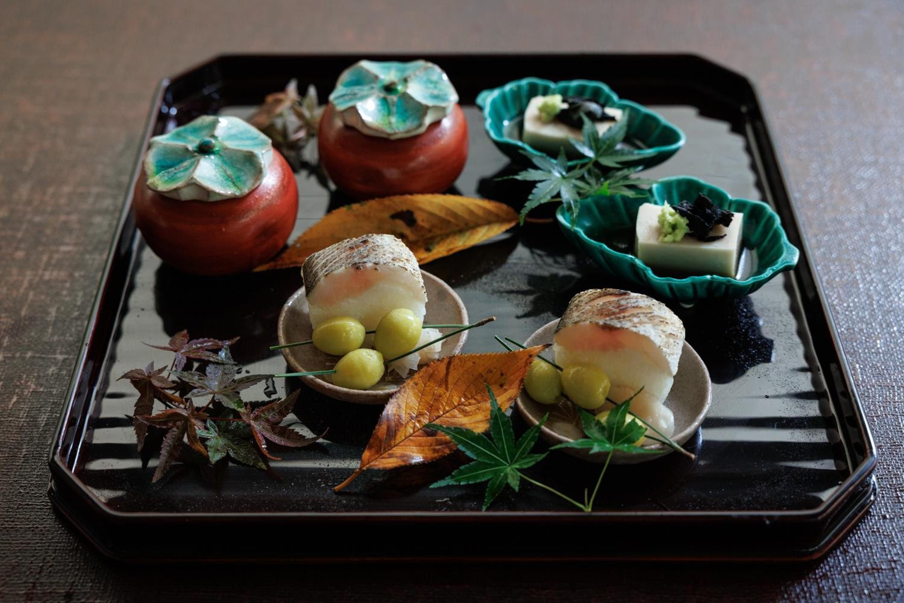 Artfully arranged seasonal kaiseki dishes arrive on black lacquerware, each element precisely positioned like jewels—from persimmon cups to delicate tofu nestled in jade-colored bowls.