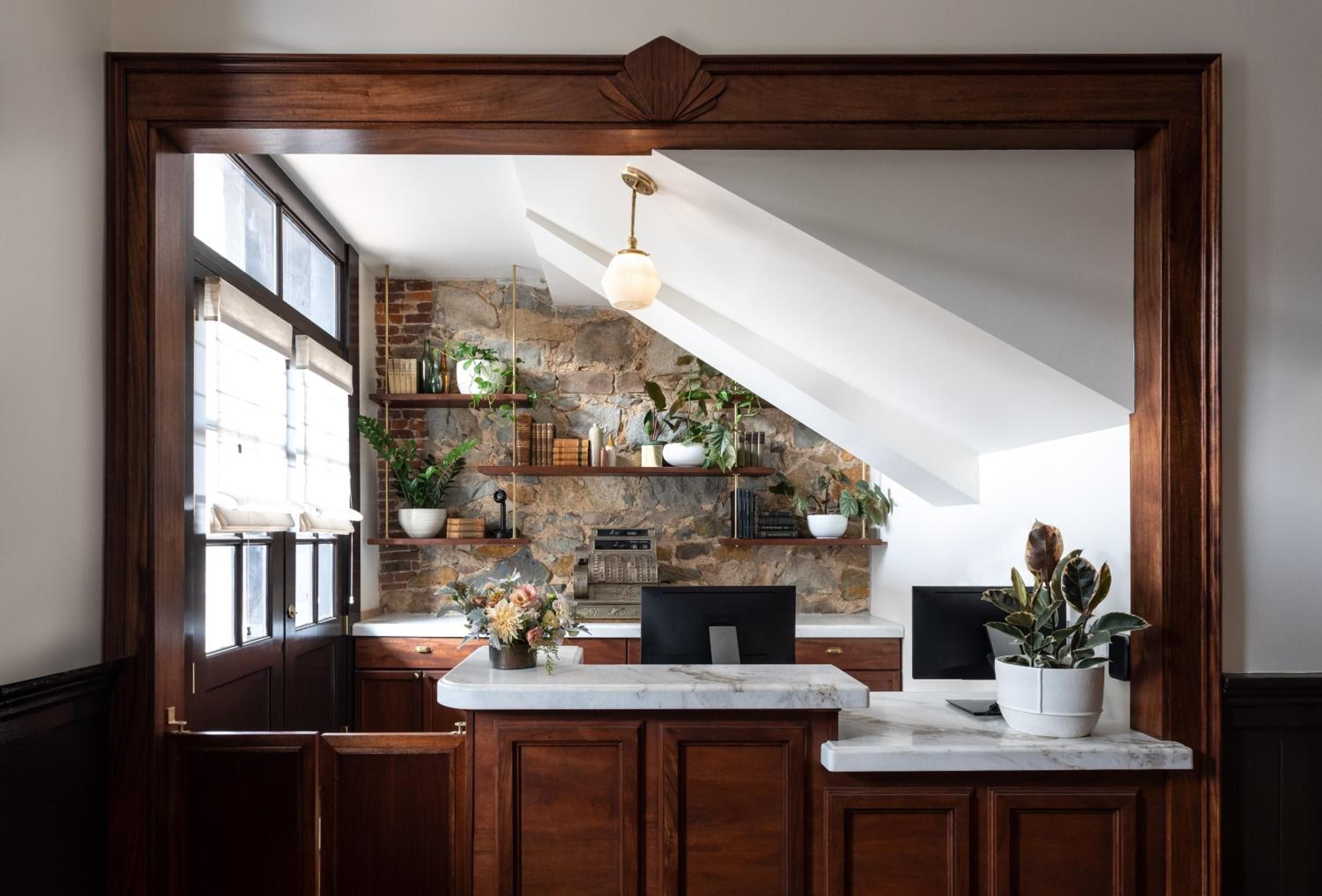 Warm wood frames reveal a sophisticated kitchen where exposed stone walls meet marble countertops, creating an inviting culinary sanctuary beneath slanted ceiling beams.
