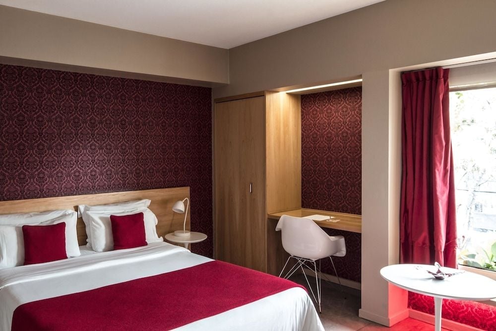 Rich burgundy damask wallpaper creates intimate drama while natural wood tones and crimson accents strike an elegant balance in this thoughtfully appointed guest room.