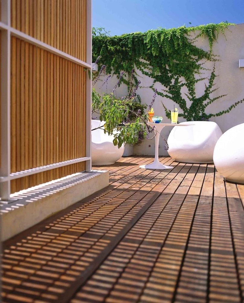 Vine-draped walls frame the rooftop terrace where sculptural white seating catches afternoon shadows cast by bamboo screens, creating an urban oasis above Buenos Aires.